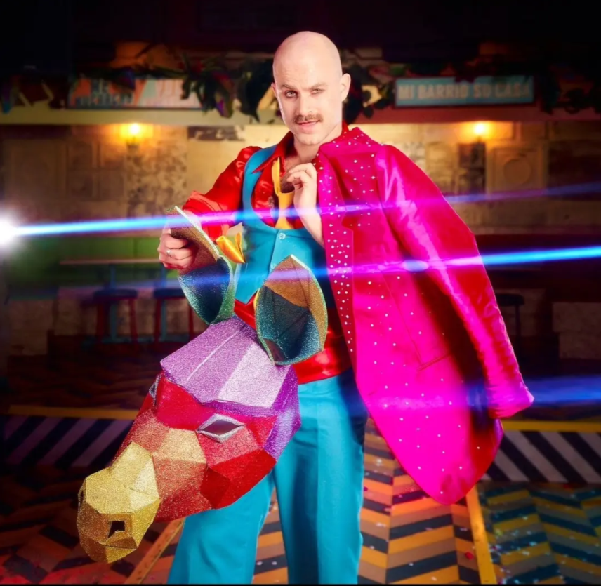 A person dressed in colorful costume holding a Minecraft-themed prop, standing in a vibrant indoor setting.