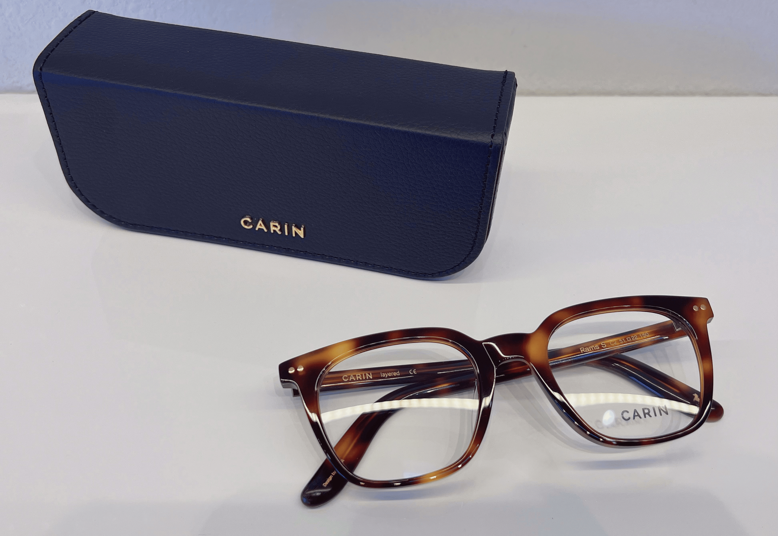 Brown tortoiseshell eyeglasses with a blue CARIN case on a white surface.