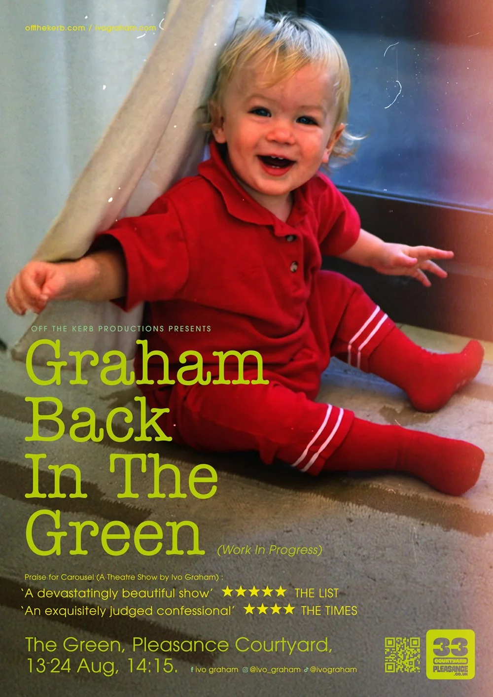 A young child with blonde hair, wearing a red outfit with red tights, sitting on a carpeted floor, smiling and laughing, next to a door or window.