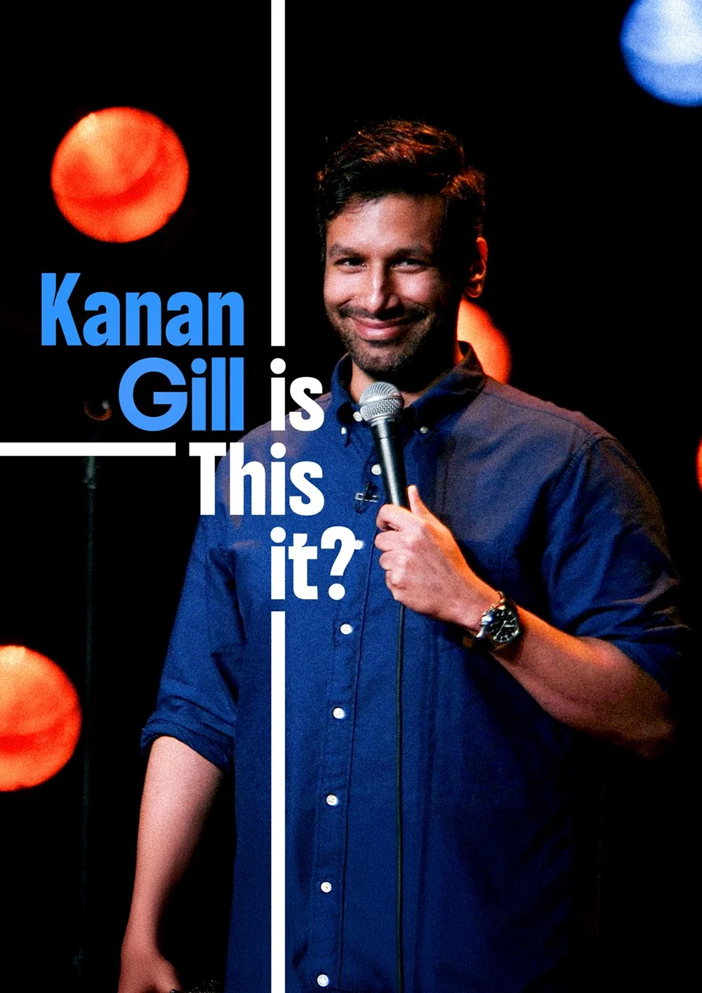 Stand-up comedian Kanan Gill holding a microphone on stage with a dark background, illuminated by red and blue spotlights, smiling. Overlaid text reads 'Kanan Gill is this it?'