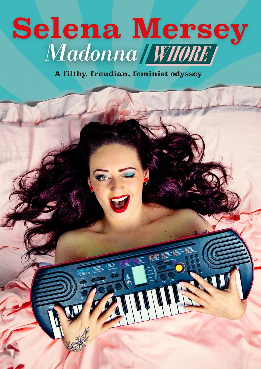 A woman lying on a pink bedspread, playing a toy keyboard, winking and smiling with red lipstick, dark makeup, and purple hair.