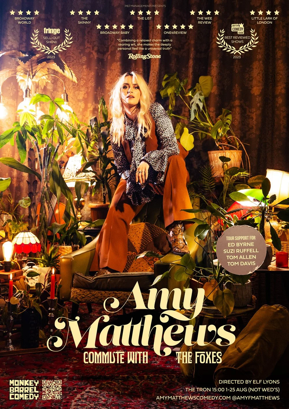 Poster for Amy Mathews show 'Commute with the Foxes' featuring a woman sitting on a chair surrounded by houseplants, candles, and lamps, with dark curtains in the background and multiple reviews and awards listed at the top.