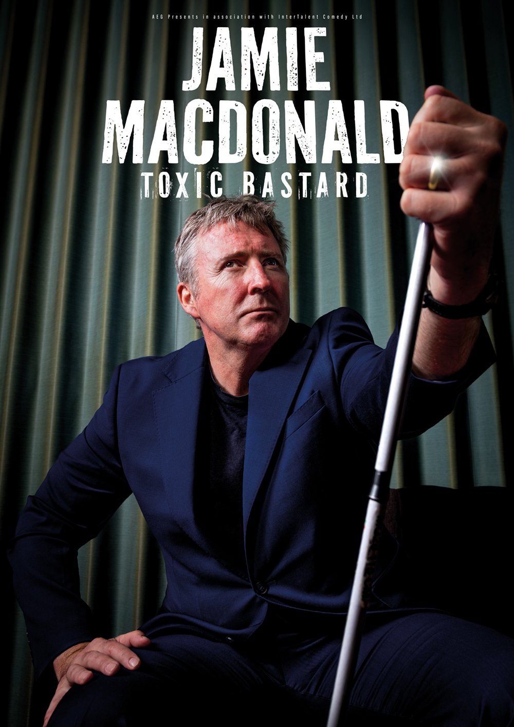 Promotional poster for Jamie MacDonald titled 'Toxic Bastard', featuring him in a dark suit holding a golf club, with a serious expression against a green curtain backdrop.