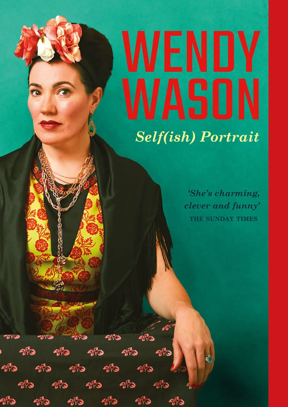 Book cover featuring author Wendy Wason wearing colorful floral headpiece, black vest, yellow and red patterned top, and layered jewelry, with a table covered in black cloth with pink floral pattern in front; red and teal background with book title a