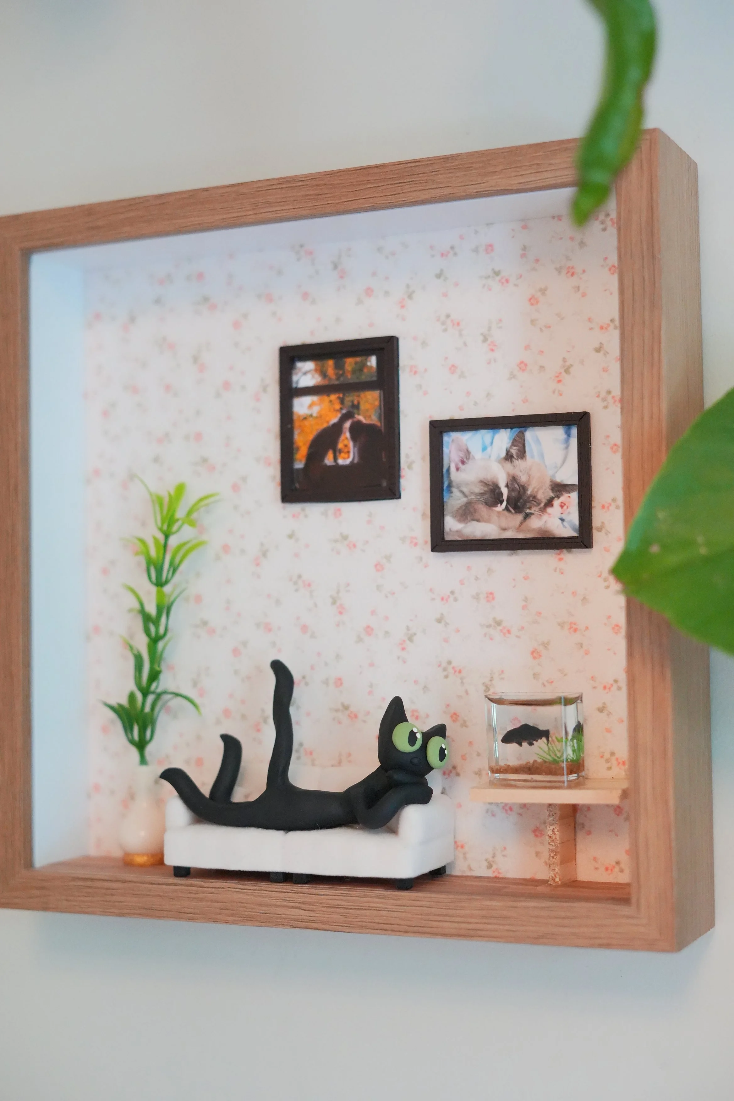 Miniature room display with black cat figurine, a green plant, framed cat photos, and a small transparent container with a fish. tiana lenos portland saturday market local artist. tiana's clay. kiwi the cat. #therapy