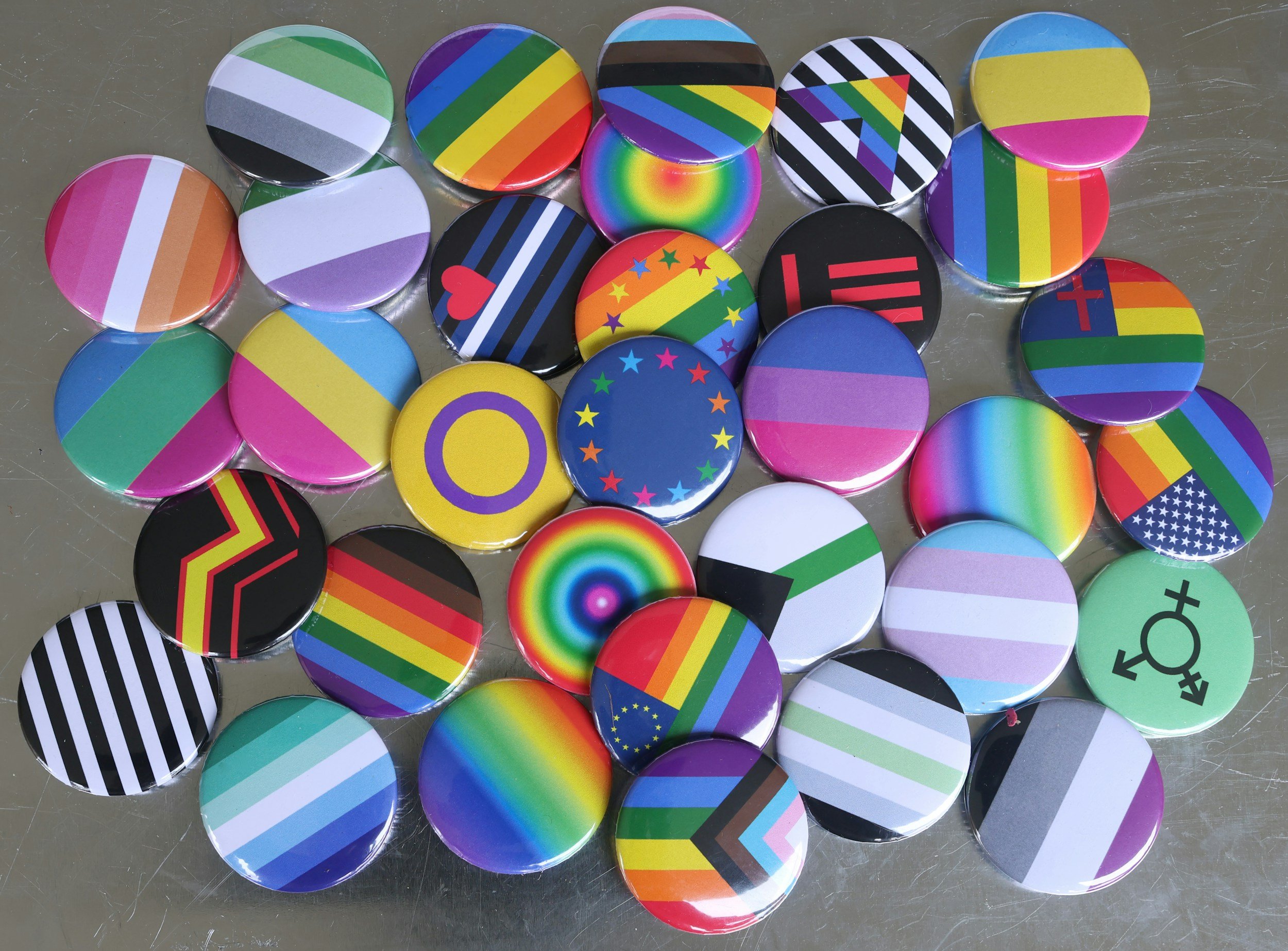 Collection of circular buttons featuring various rainbow and pride flag designs and symbols on a metallic surface.