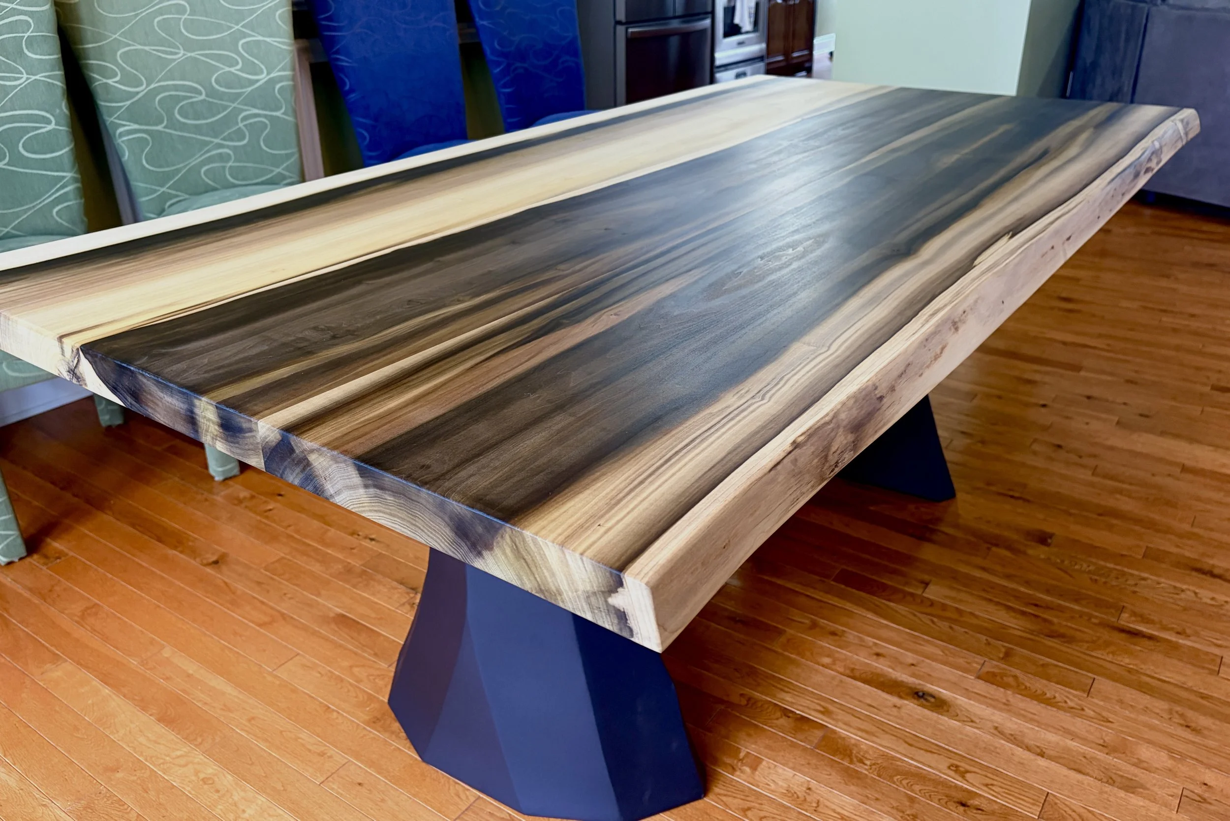  A wooden table with metal legs against a wooden paneled wall. This table has a dark epoxy river down the center.