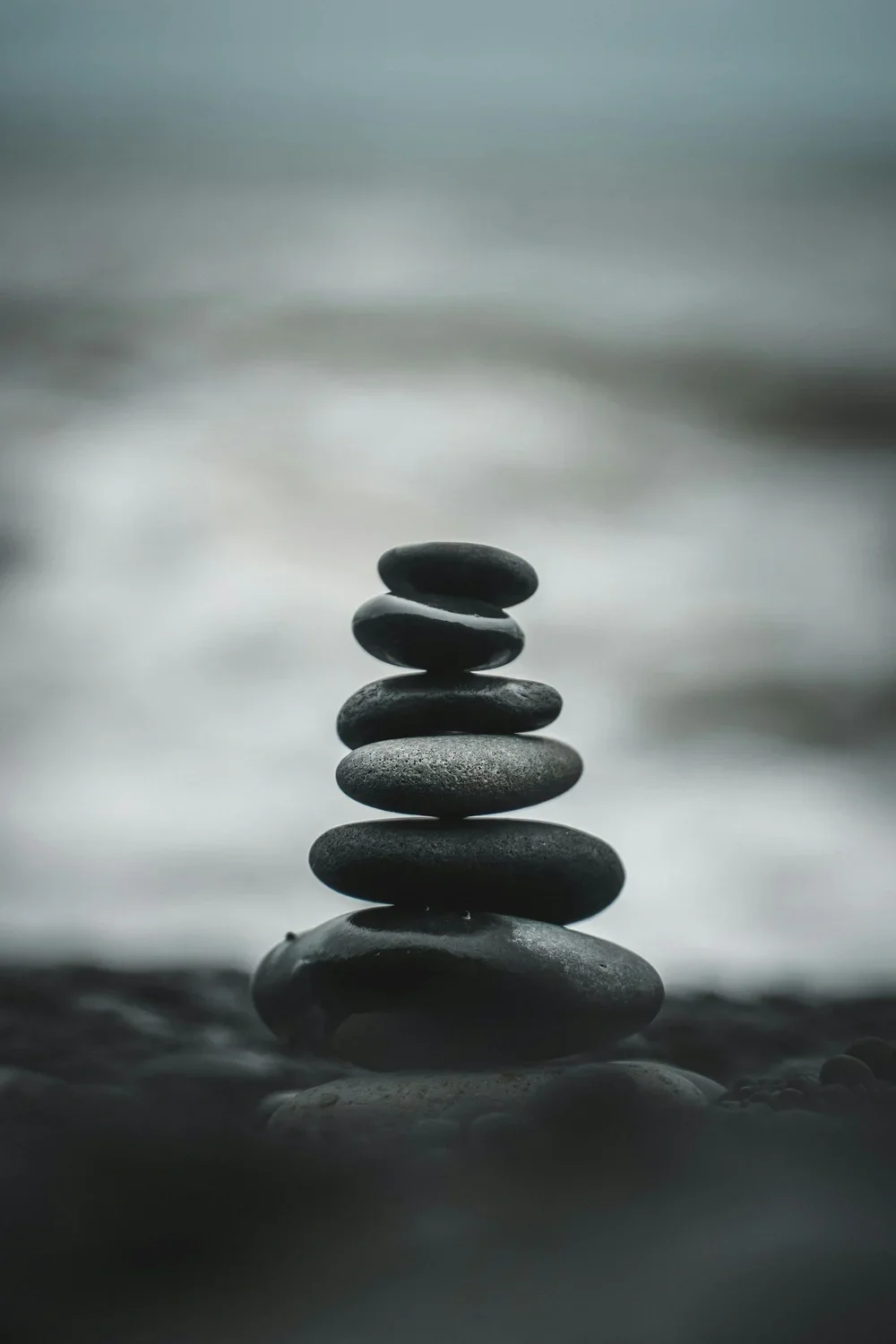 Stacked smooth black stones on beach with blurred ocean background