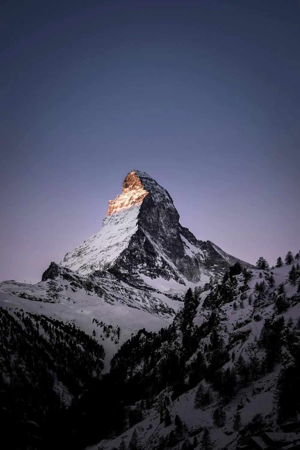 Snow-covered mountain with a sharp peak against a dusky sky.