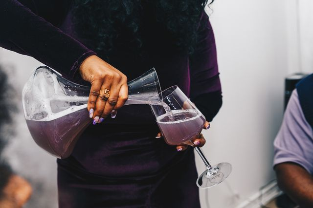 Person pouring a purple beverage from a pitcher into a wine glass at a gathering.