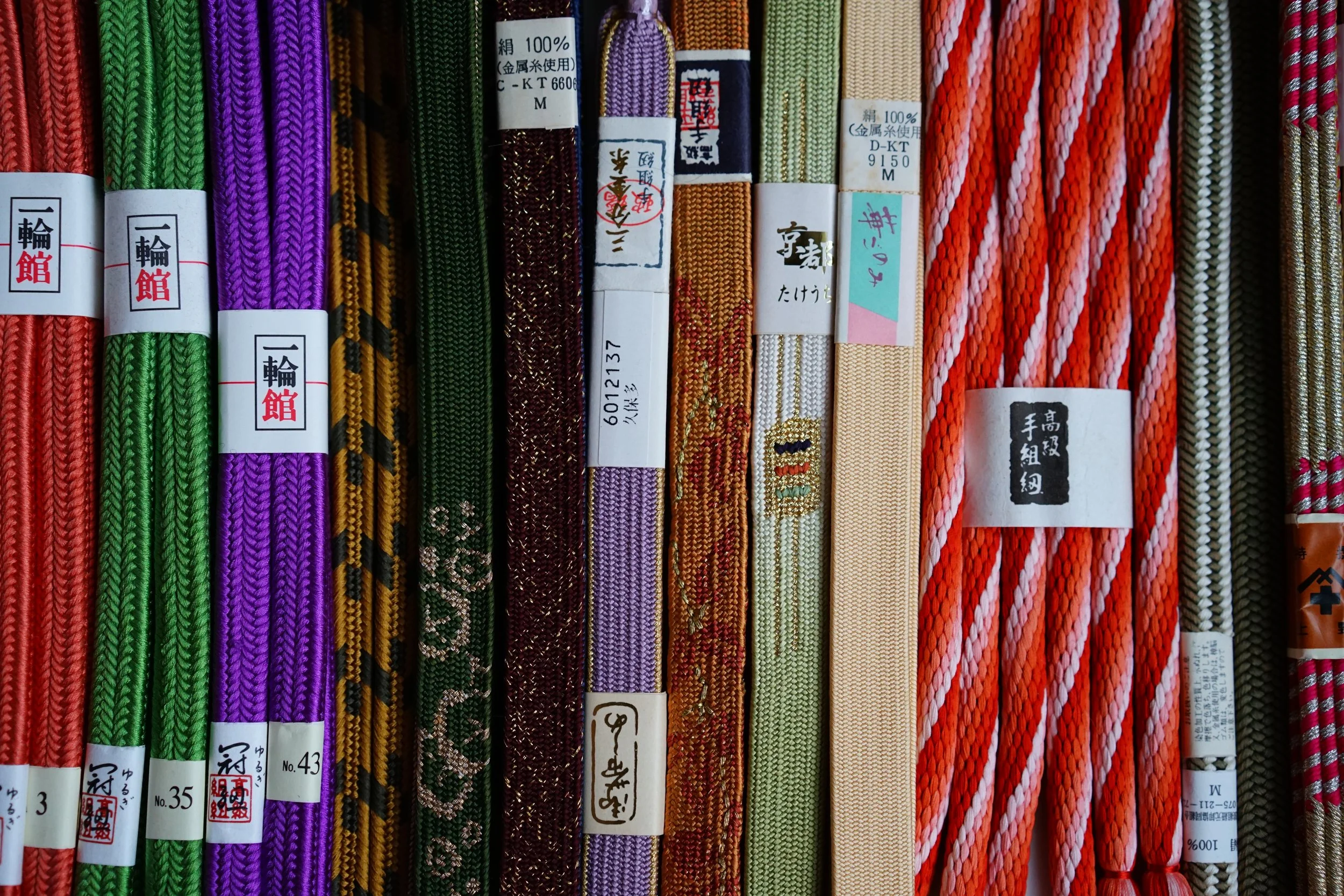 Vintage colourful woven cords or ribbons arranged vertically, with original Japanese labels and tags attached.