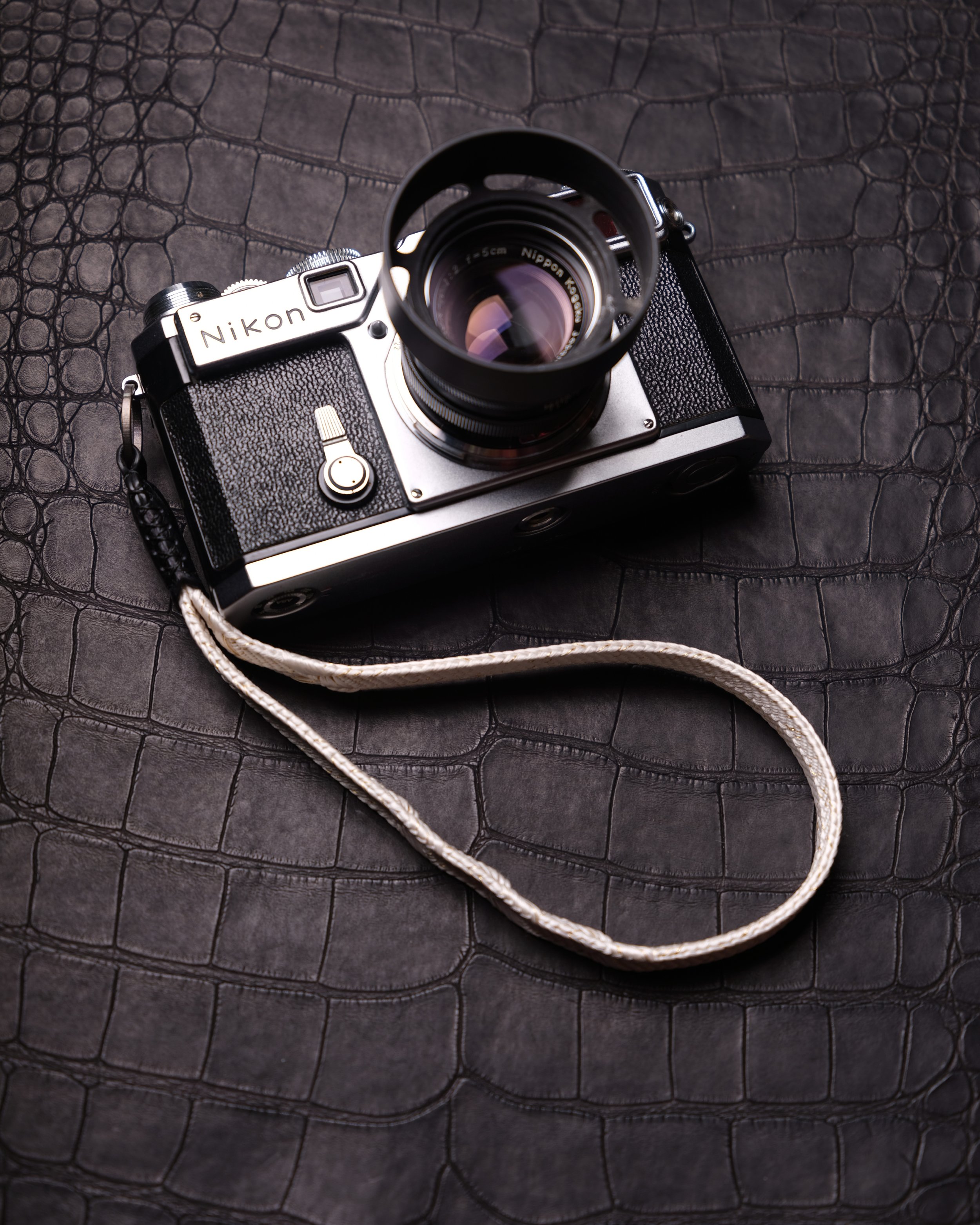 A vintage Nikon film camera with a lens and strap placed on a textured black leather surface.