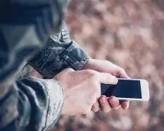 Person holding a smartphone outdoors with fallen leaves in the background.
