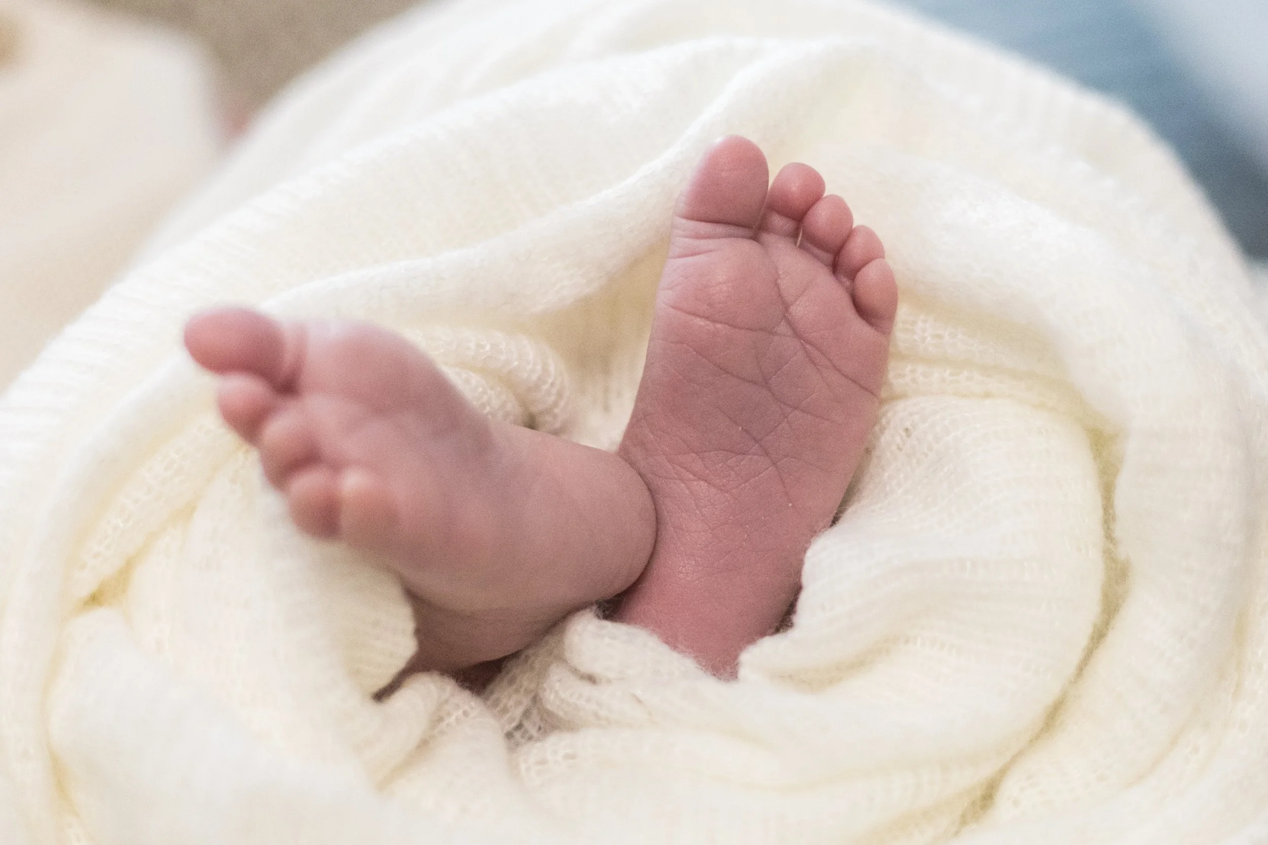 Ein winziger Babyfuß, der auf einem weichen, cremefarbenen Tuch liegt.