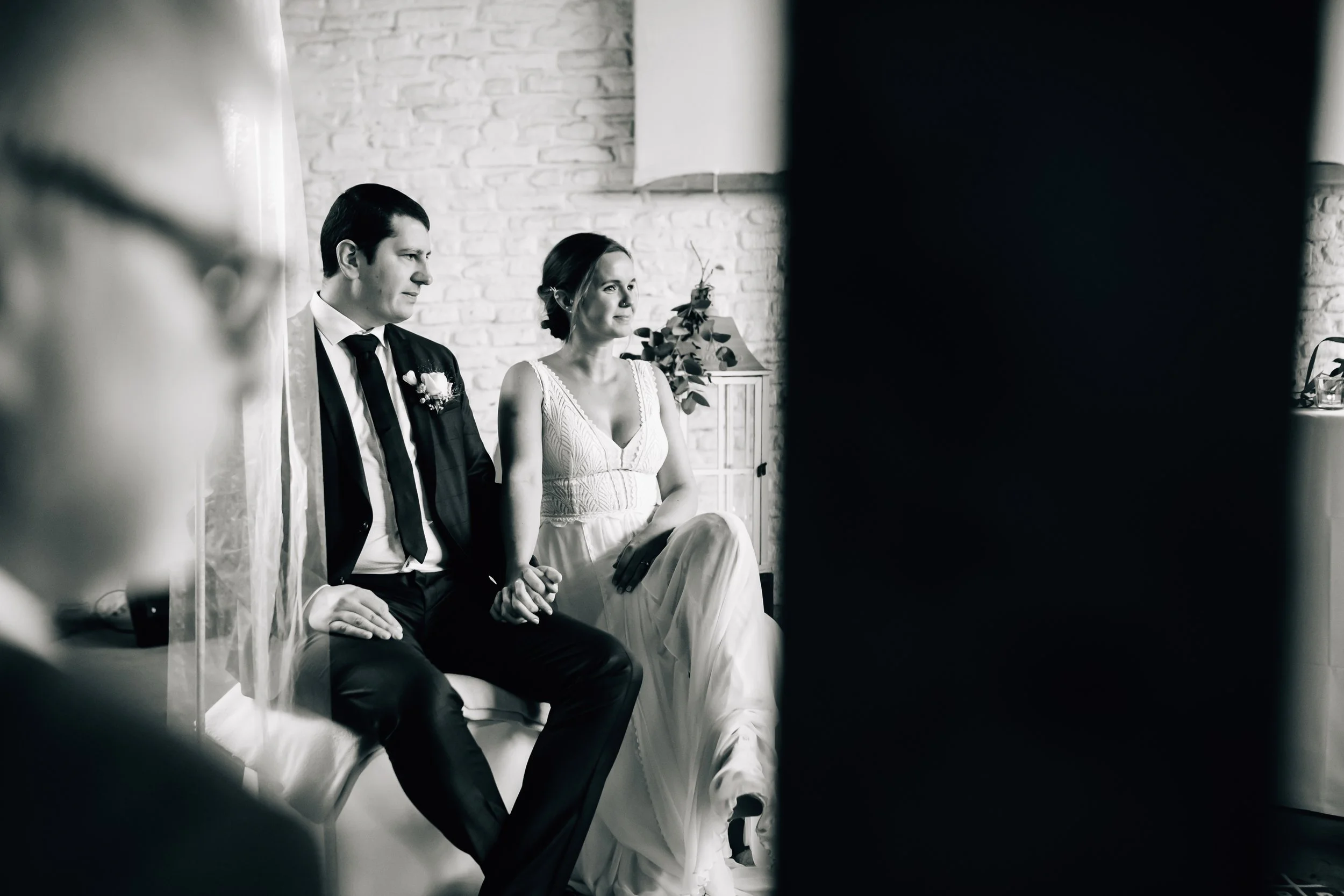 Braut und Bräutigam sitzen während der Trauung in einem Raum mit weißer Steinwand