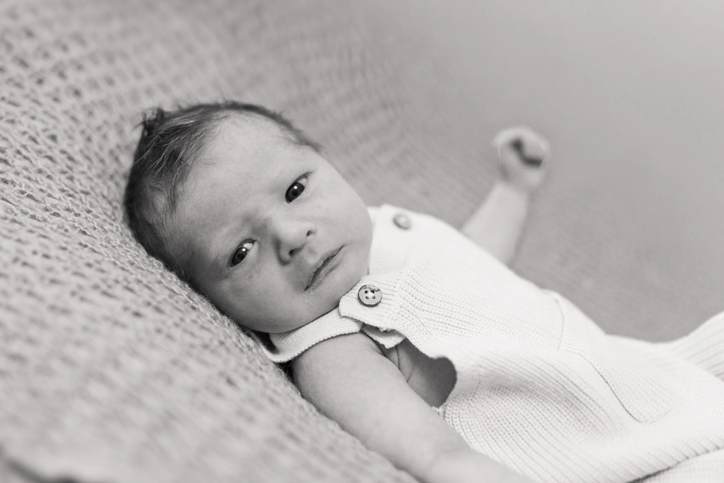 Nahaufnahme eines Babygesichts, liegend auf einer Couch, schwarzen und weißen Tönen, Baby trägt ein weißes Oberteil mit Knöpfen.