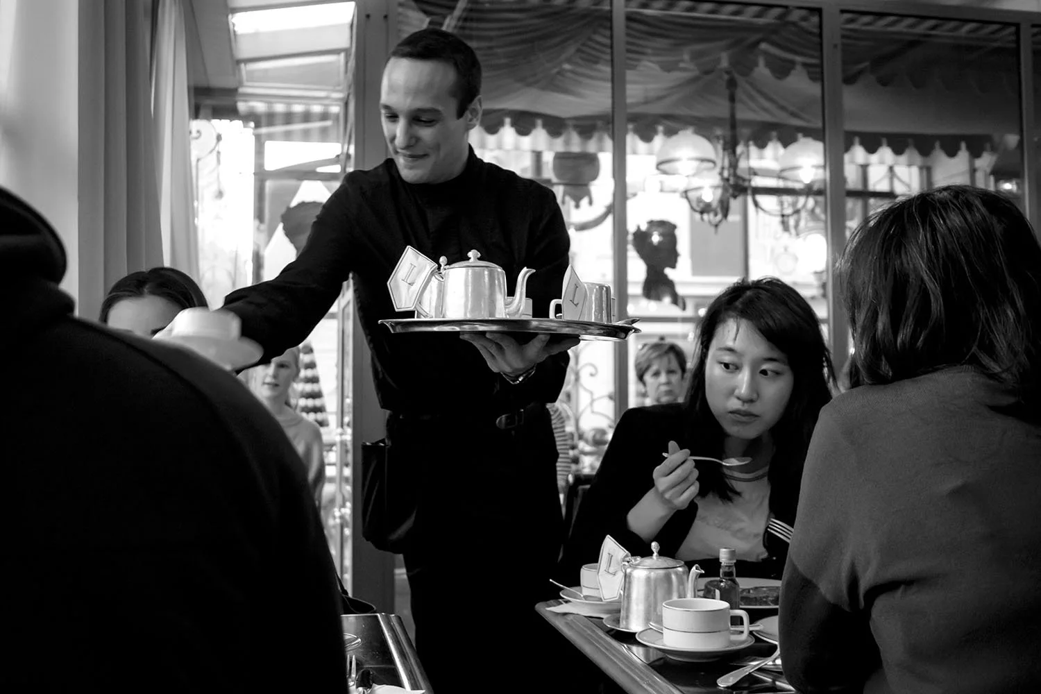A waiter serves tea while guests settle into their conversations inside the café.
Paris