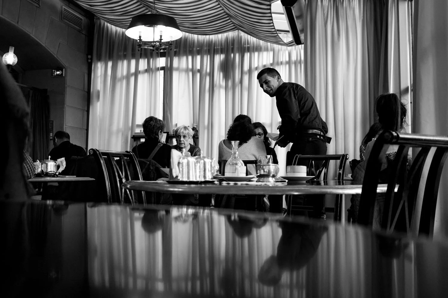 Inside a café, a waiter serves tea as conversations unfold quietly around the room.
Paris