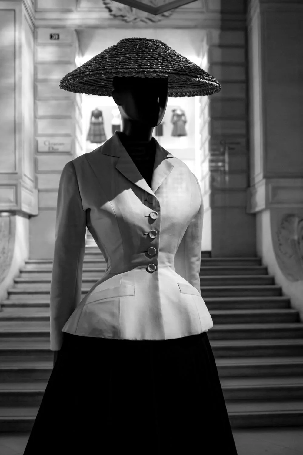 The iconic Dior silhouette stands quietly before the staircase, echoing the enduring elegance of the house.
