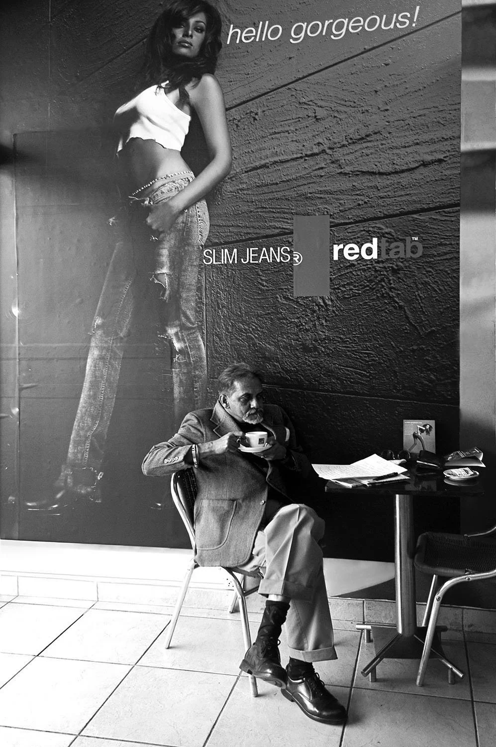 A quiet coffee moment unfolds beneath a striking advertisement, where everyday life meets the imagery of modern consumer culture.
Kolkata