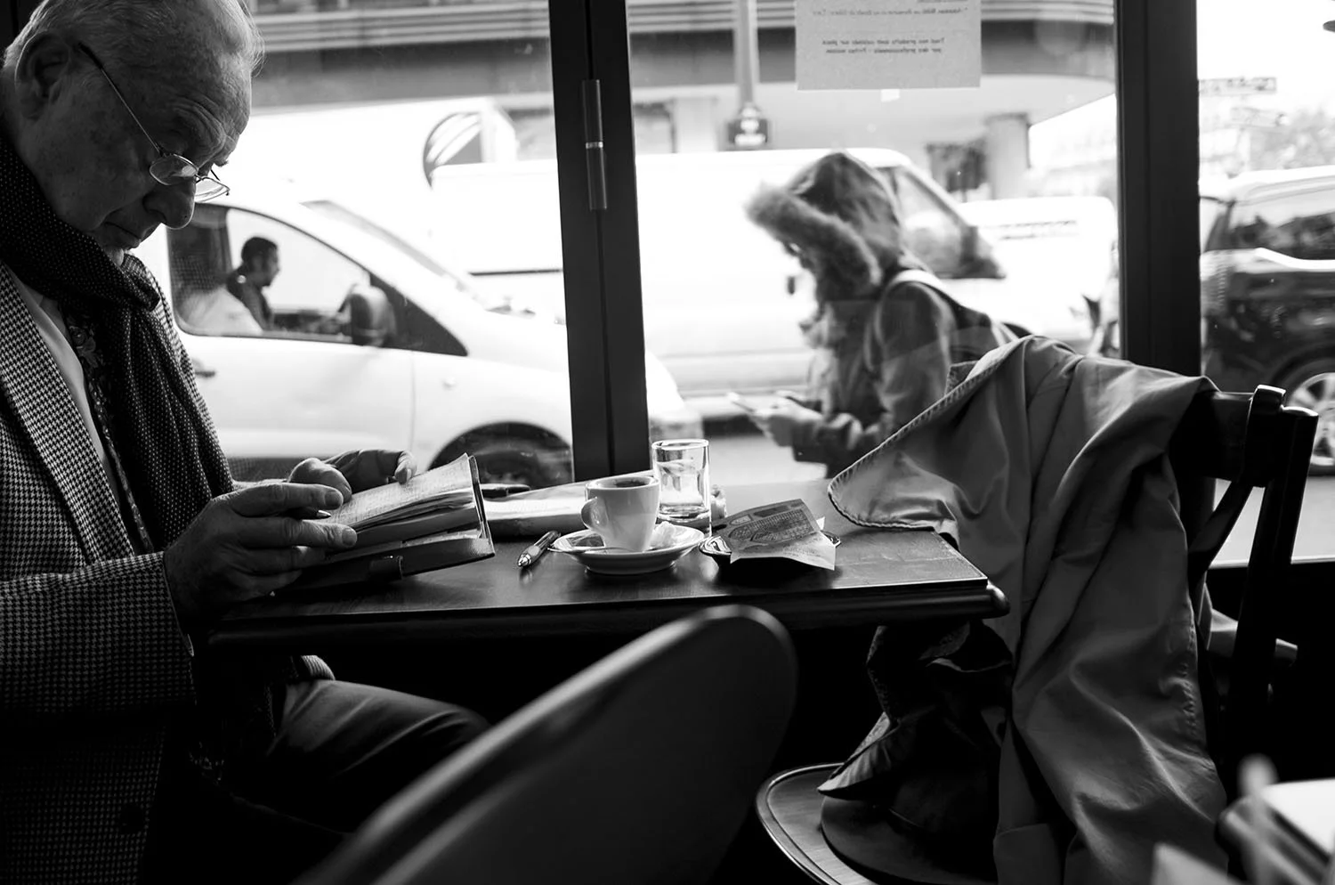 Man reading a book while drinking coffee by a café window. 
Paris