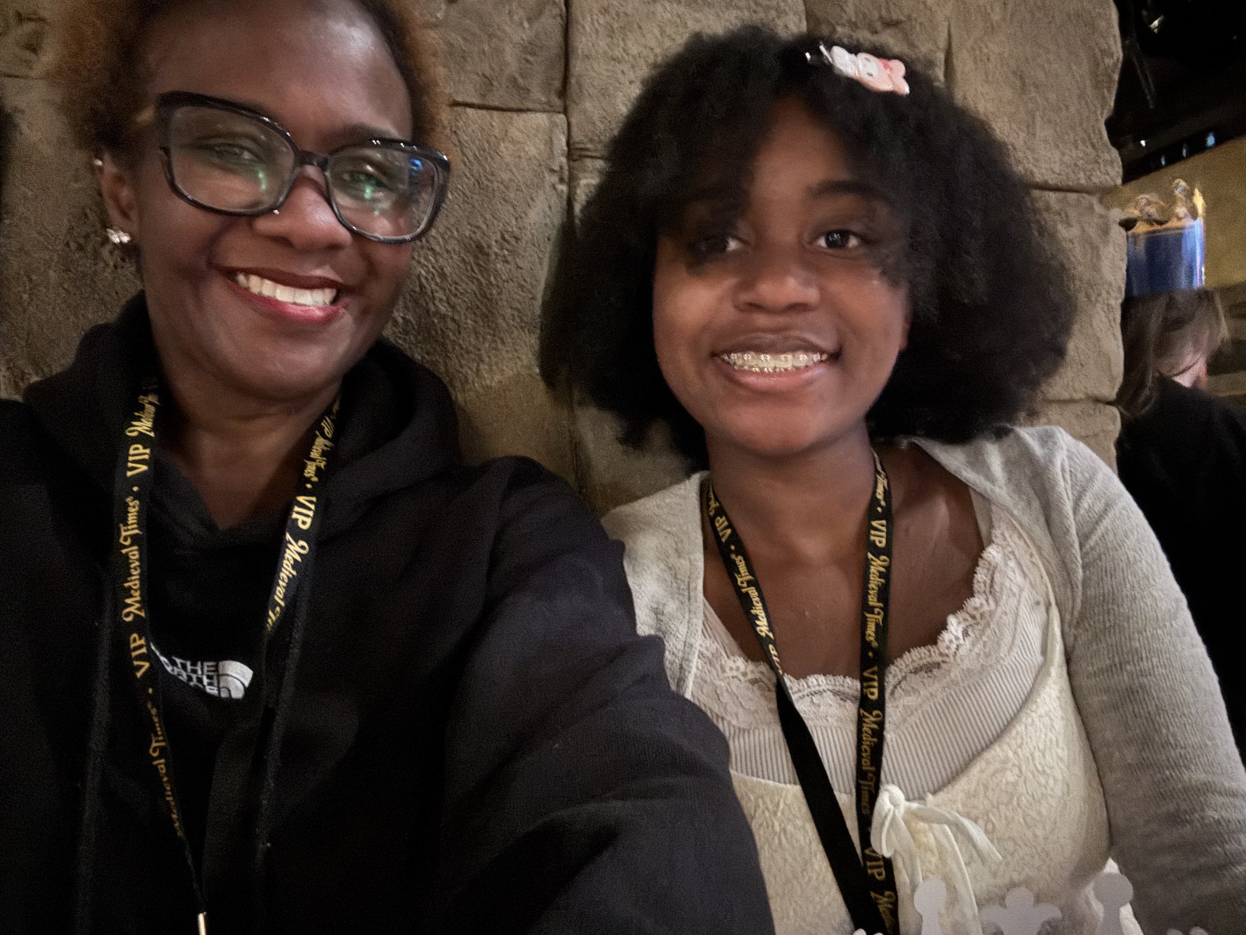 Two women smiling for a selfie in a dimly lit indoor setting. Both are wearing VIP lanyards around their necks.