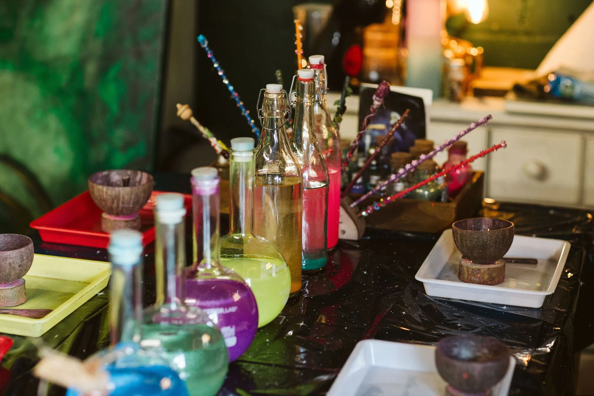 Potion bottles and small bowls on a table, with various art supplies and a cabinet in the background.