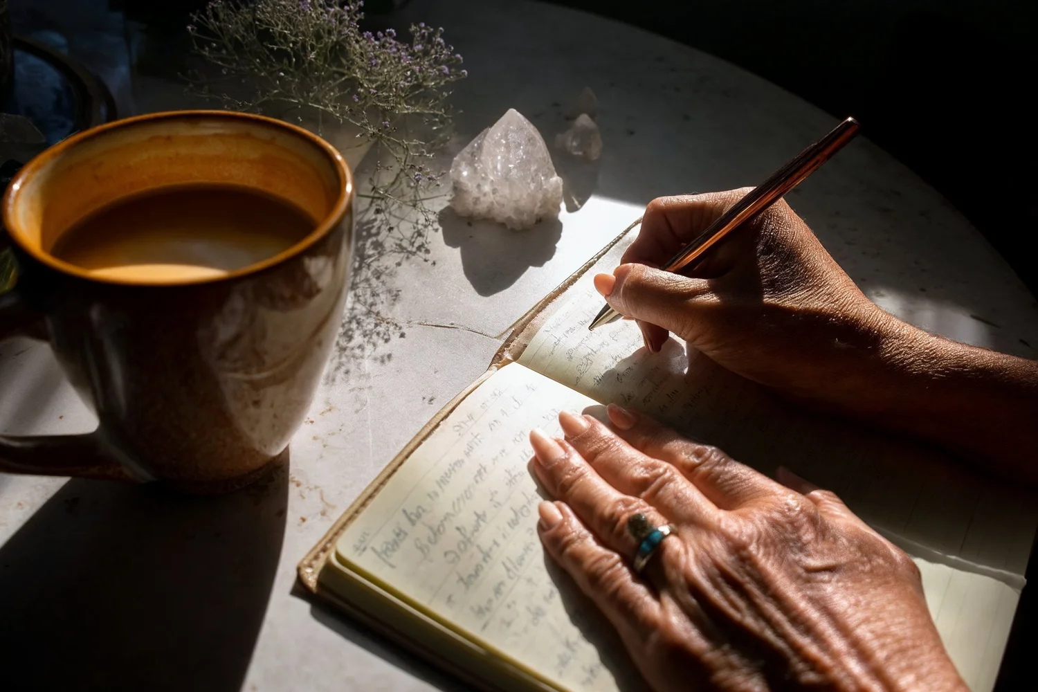 Crystals and flowers beside a journal and a warm drink