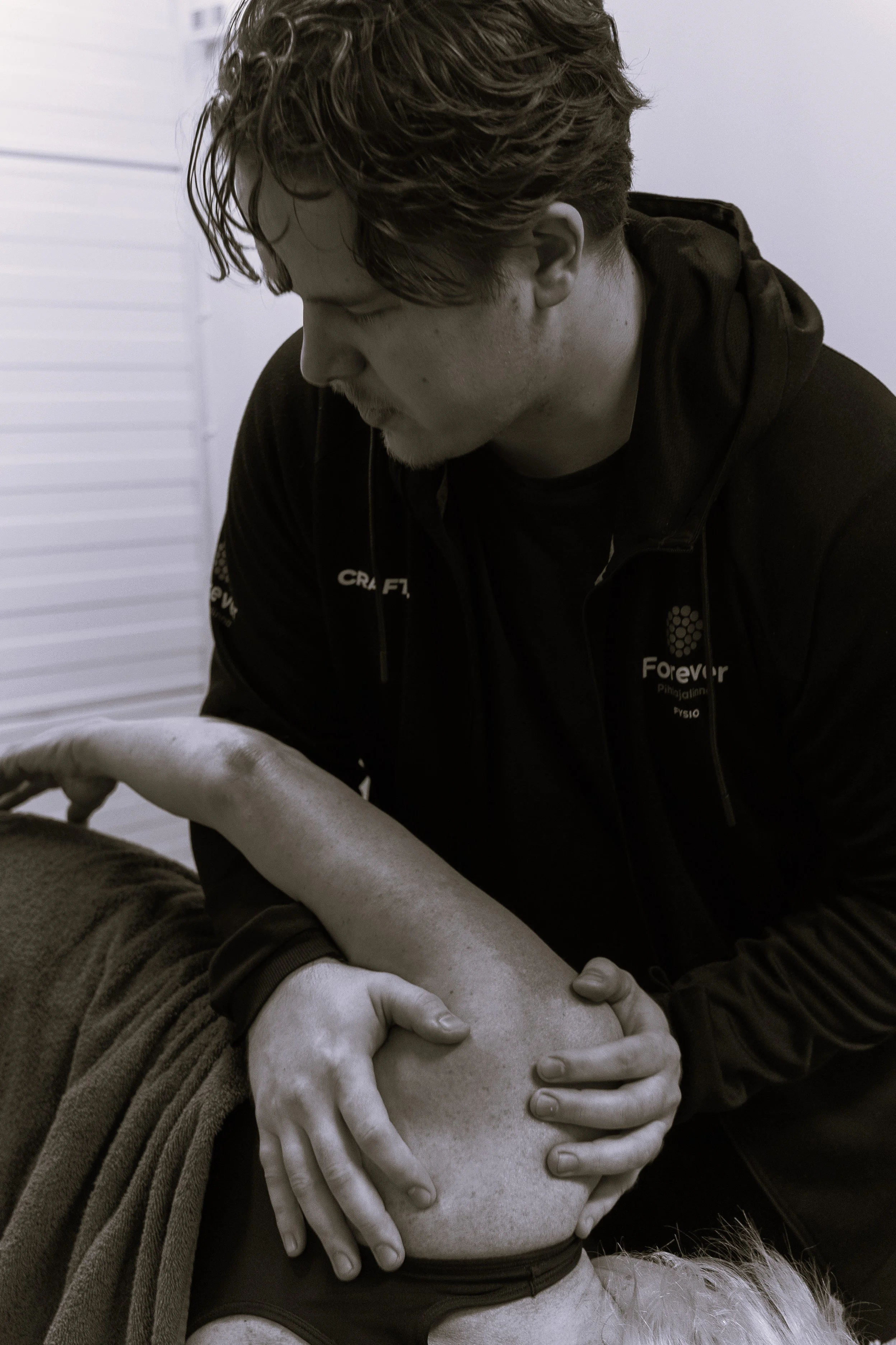 A man performs a chiropractic or physiotherapy adjustment on a person's neck or upper back, with focus on the patient's face and the practitioner's hands.