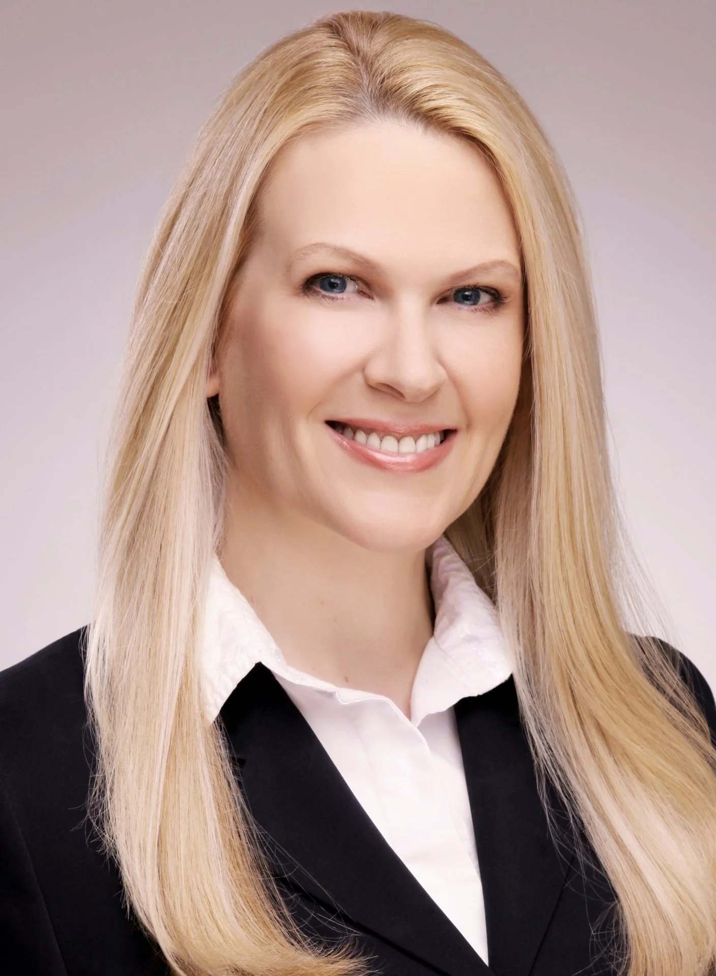 Professional headshot of a smiling blonde woman wearing a black blazer and white collared shirt