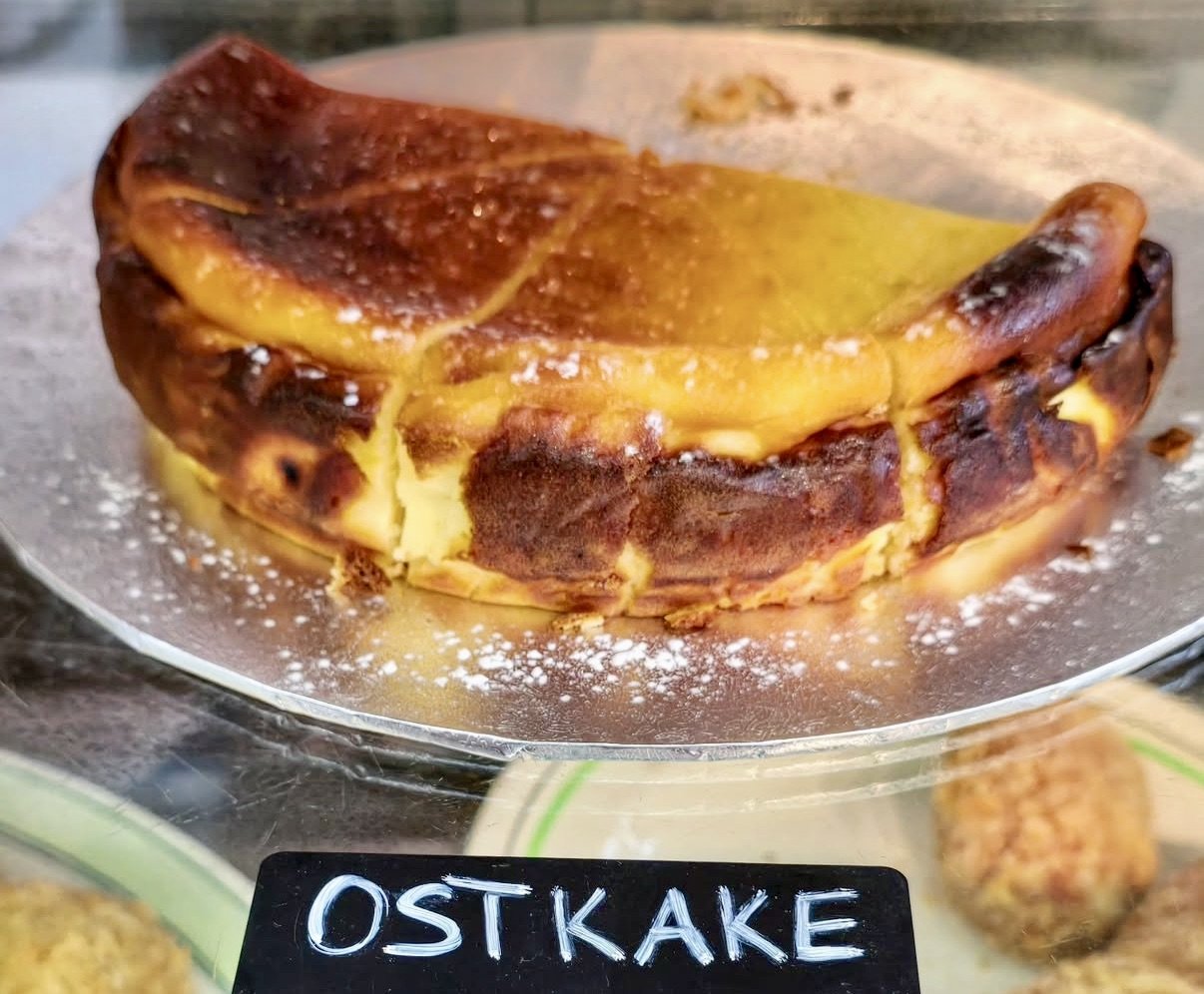 A slice of German cheesecake called 'Ostkake' with a browned crust and creamy interior, dusted lightly with powdered sugar.