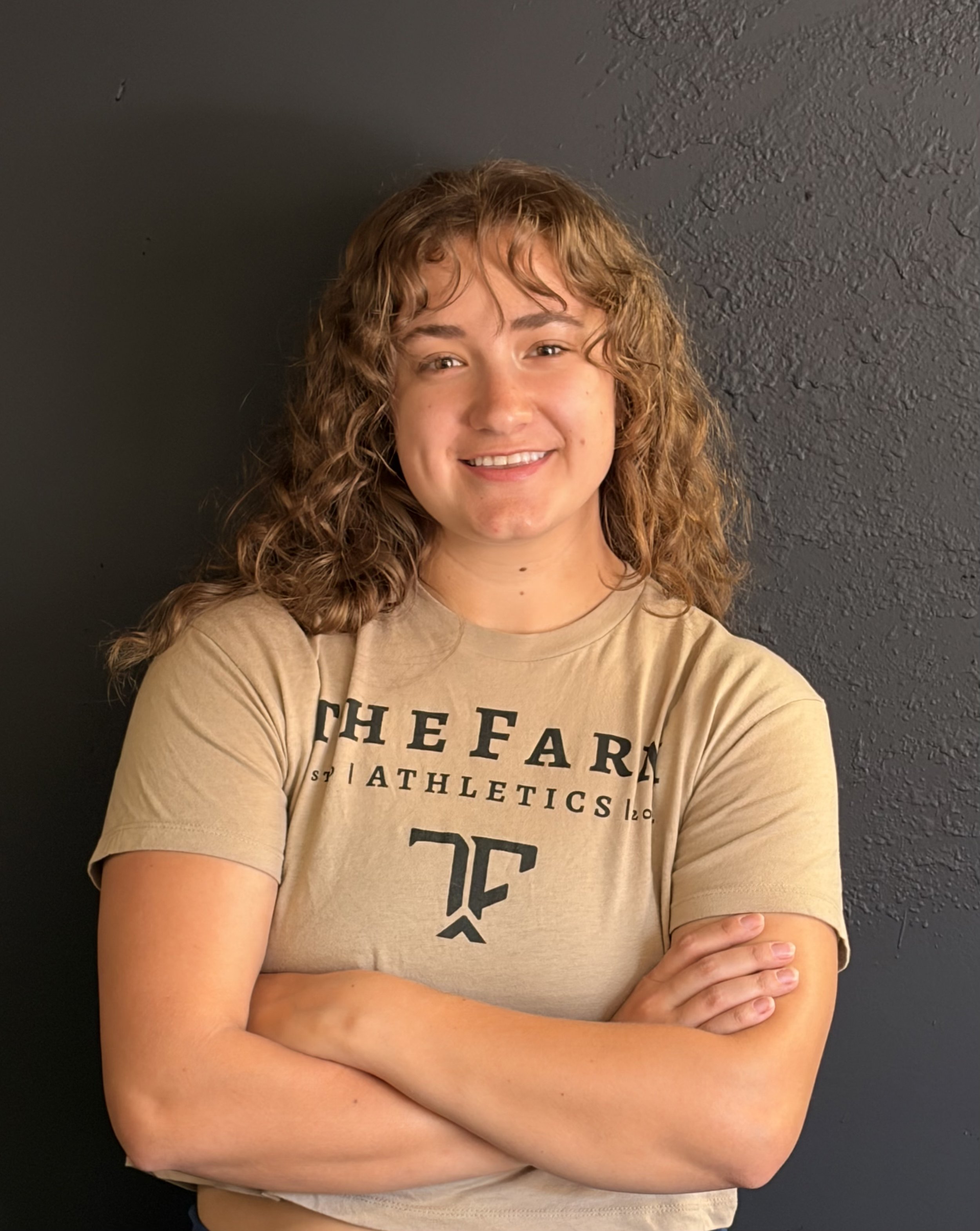 Woman with curly hair standing in front of the camera smiling for a headshot
