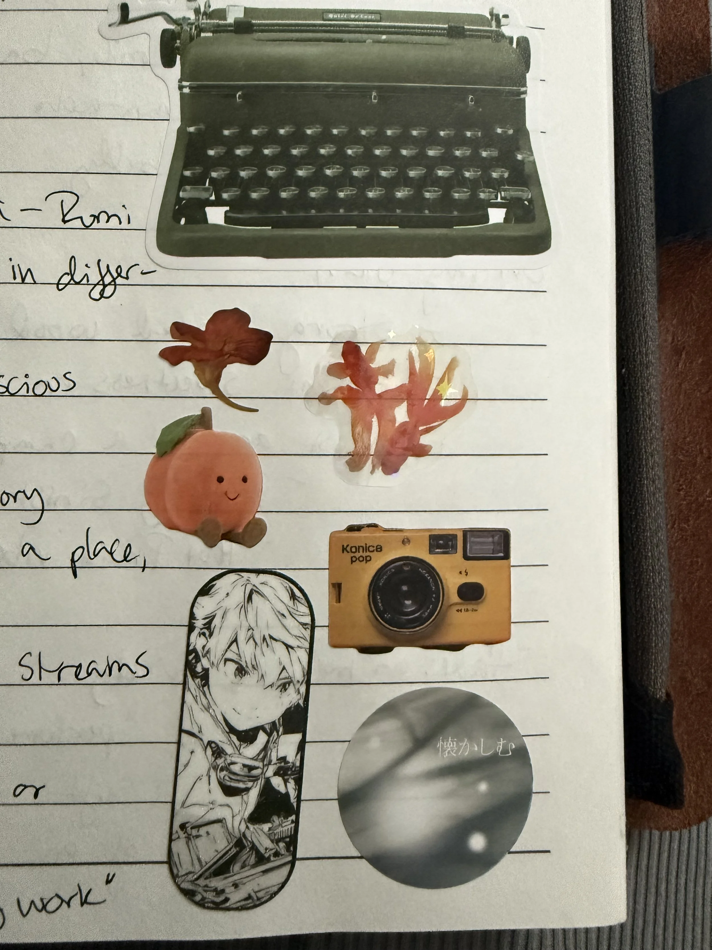 A group of stickers on a journal page: a typewriter, a flower, two goldfish, a smiling stuffed peach, a yellow camera, and an animated human figure