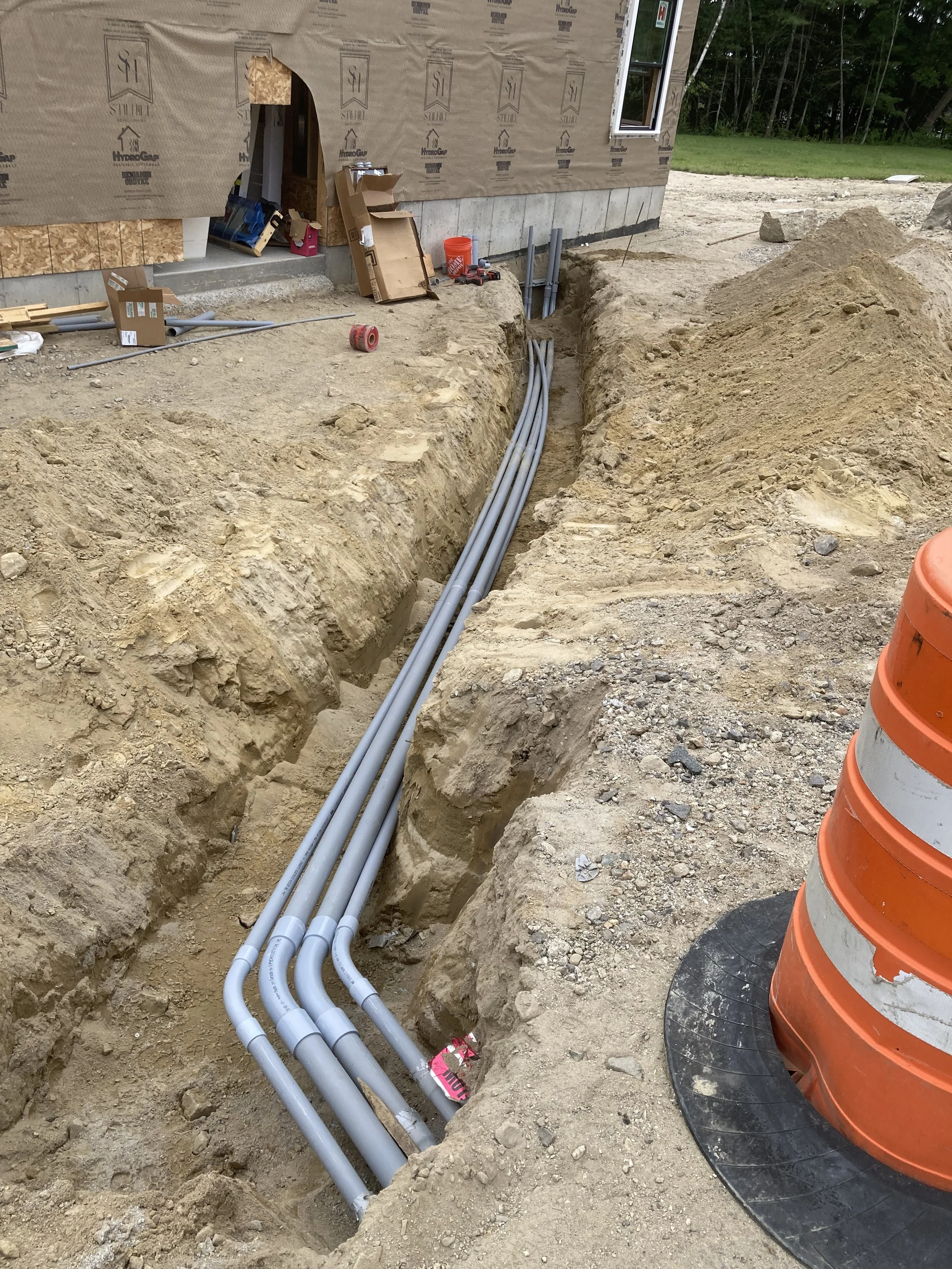 Construction site with pipes installed underground near a house under construction, with tools and building materials visible.