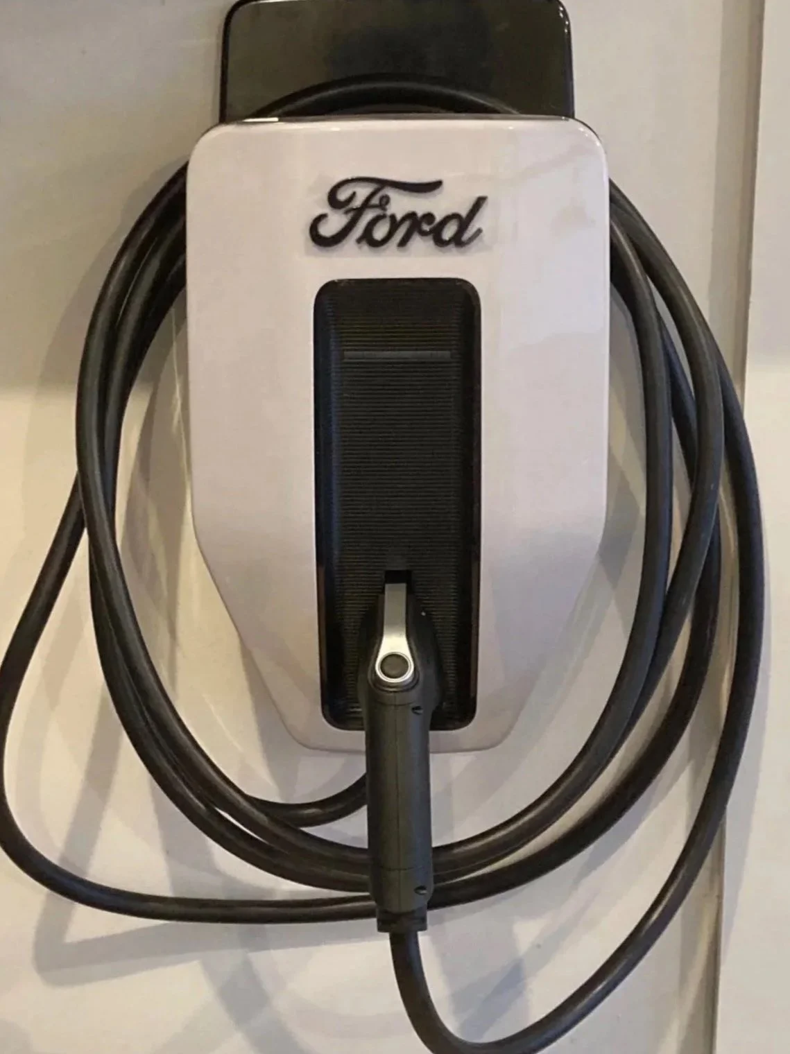 Electric vehicle charging station with a Ford logo, black charging cord, and connector.