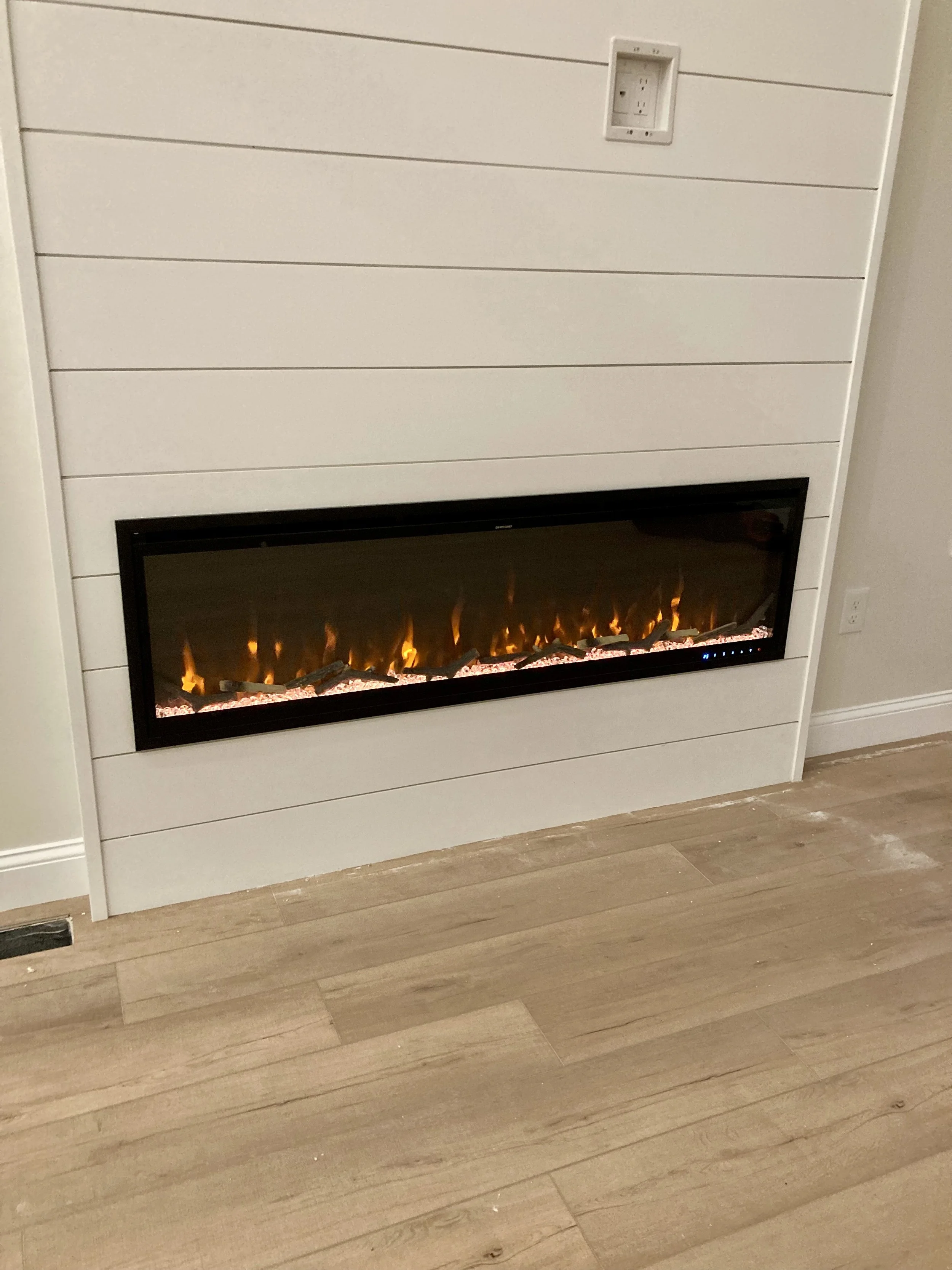 Electric fireplace built into a white wall next to a light-colored wooden floor.