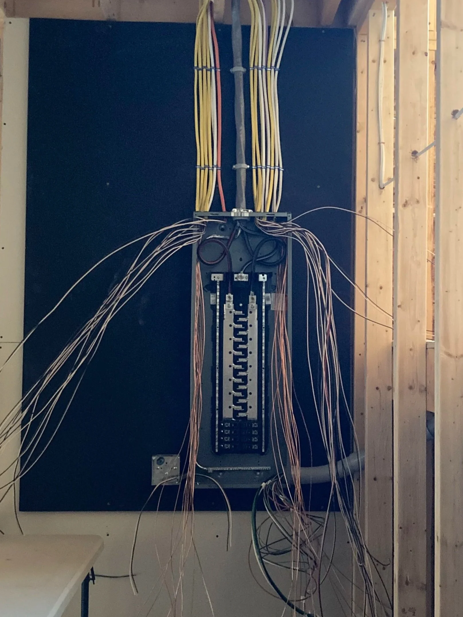 Electrical wiring panel with various colored wires organized and secured inside a wooden frame.