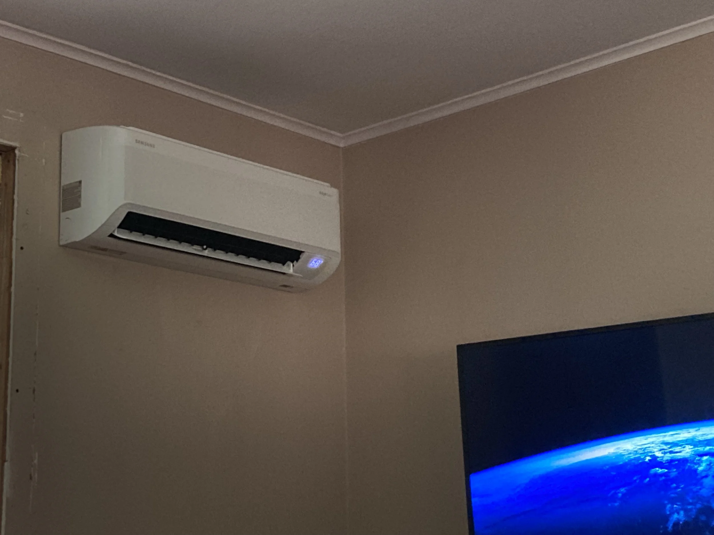 A white Samsung wall-mounted air conditioner installed on a beige wall beneath ceiling molding in a room.
