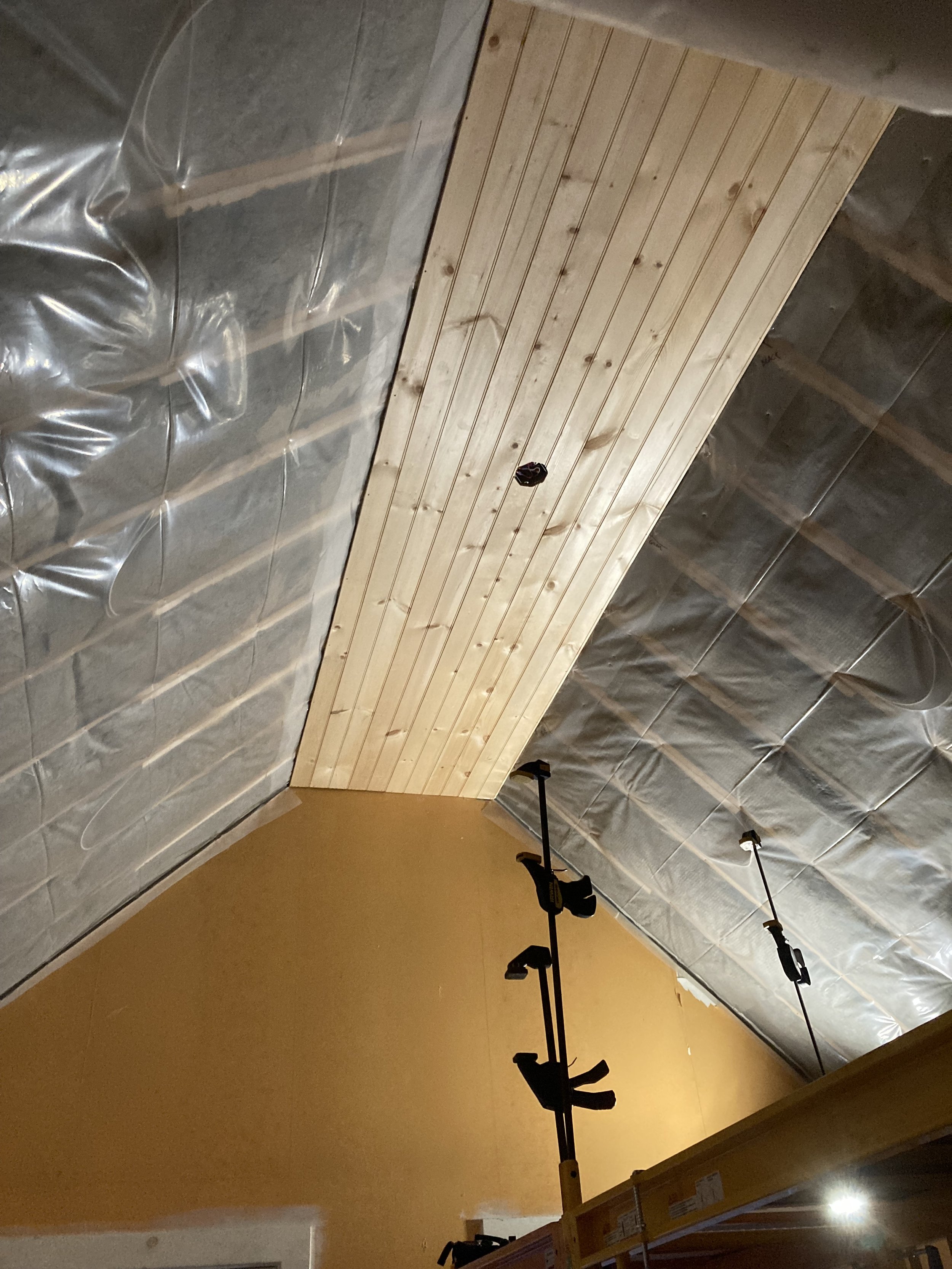 Interior of a room under construction with wood panel ceiling, metal insulation, and hanging light fixtures.