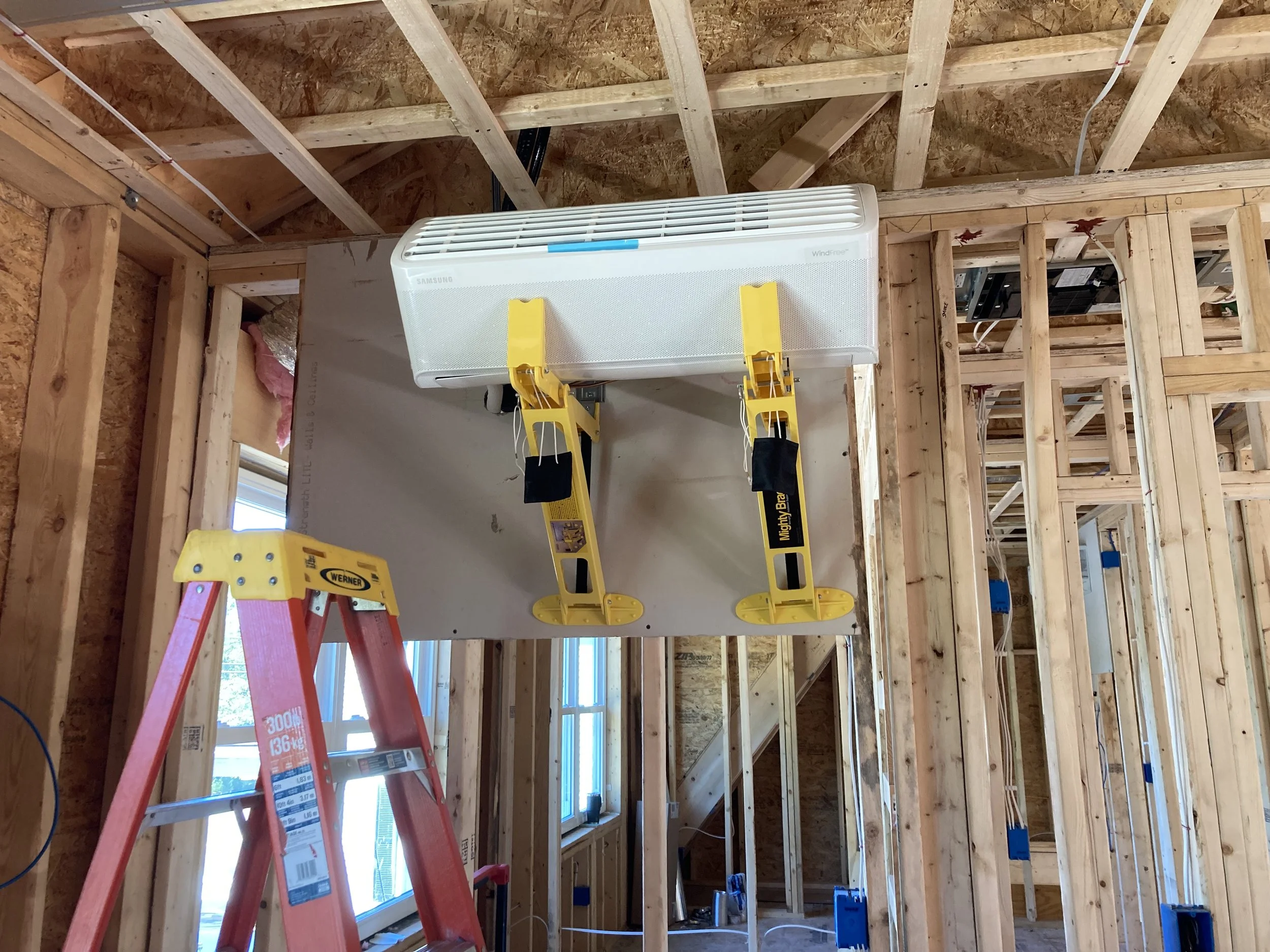 Interior of a building under construction with unfinished wooden framing, a window, and construction equipment including a ladder and a heater.
