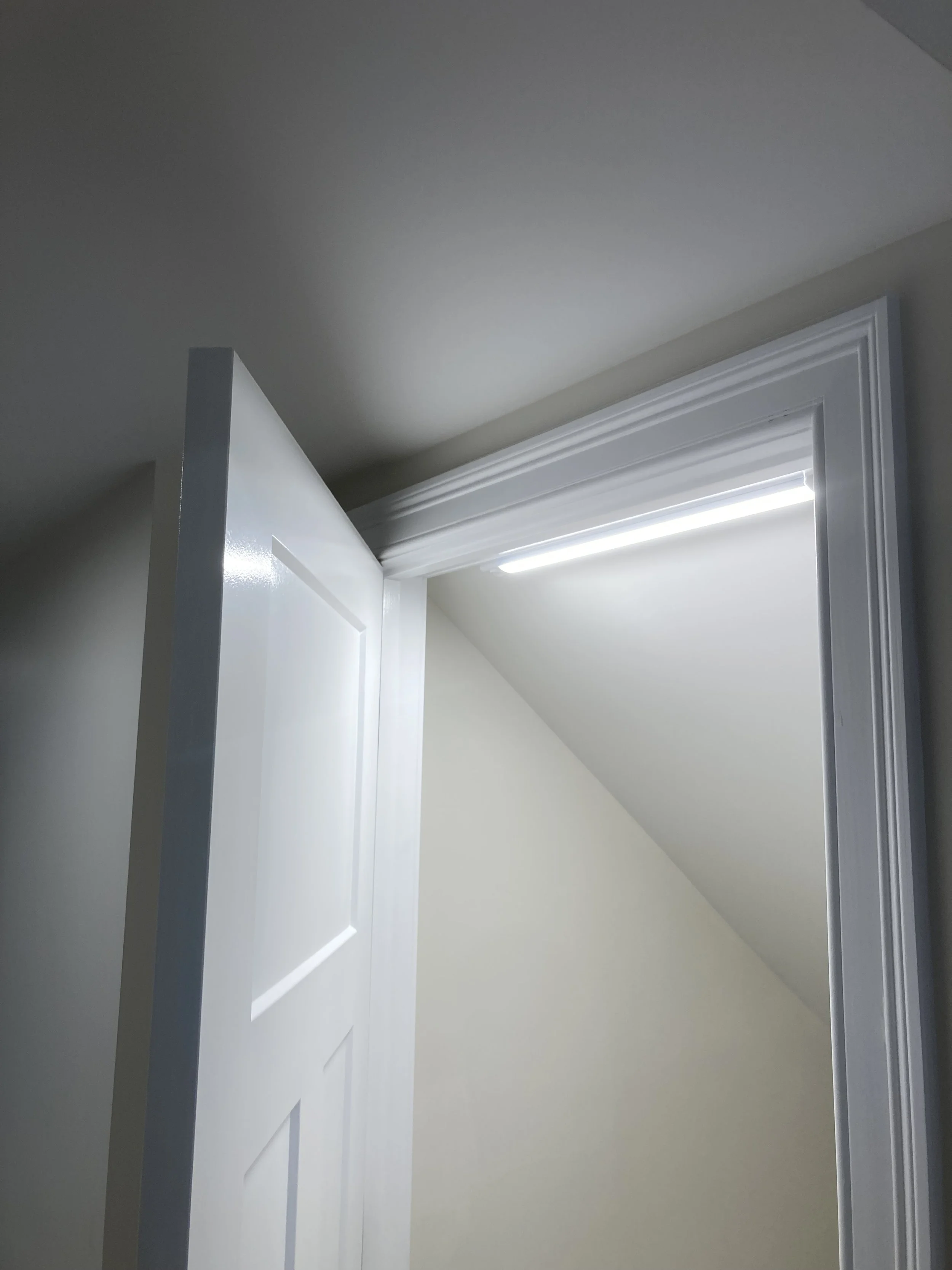 Open white door leading outside, with a sloped ceiling and LED light installed above the door frame.