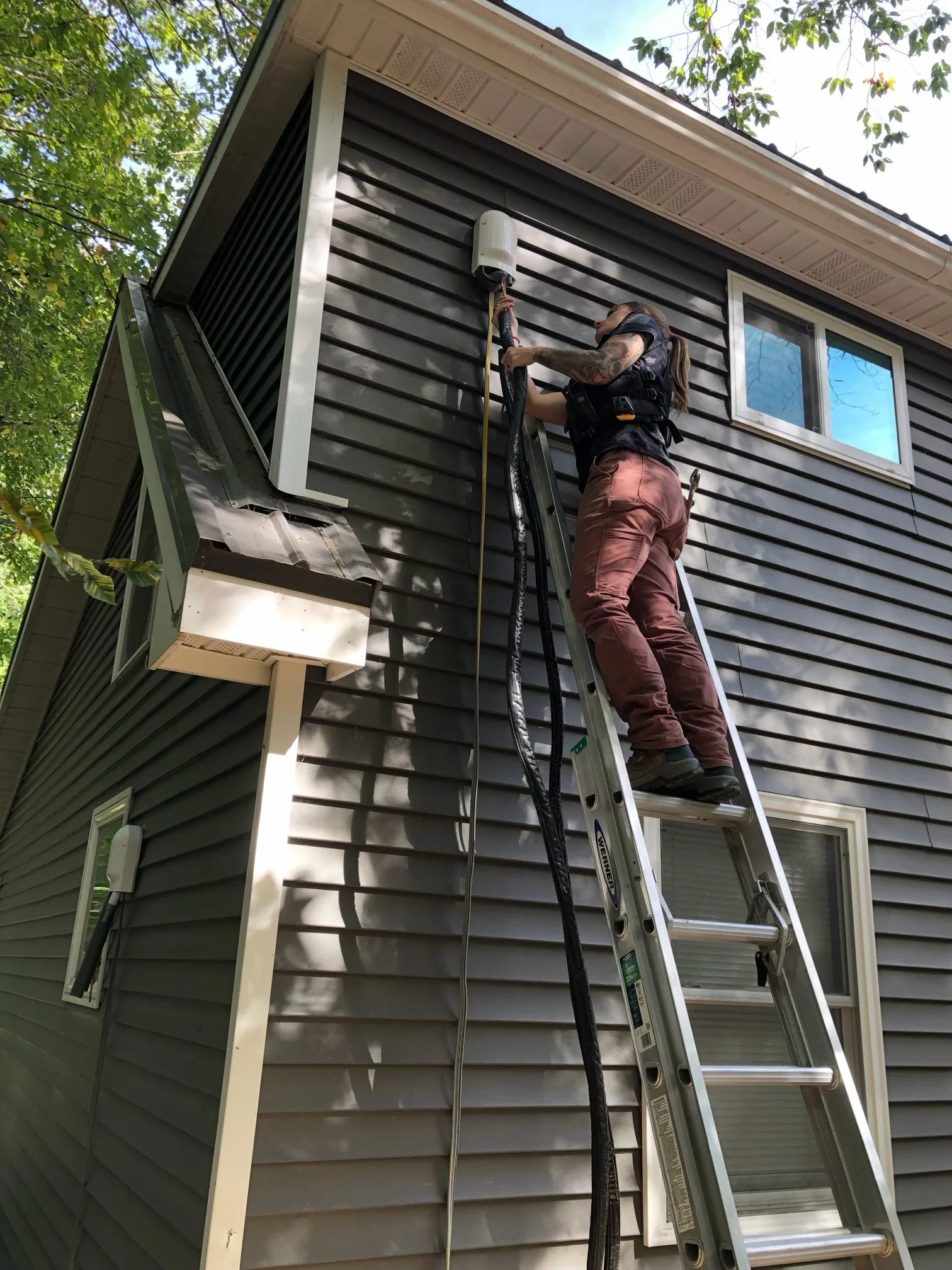 A woman standing on a ladder installing a heat pump.