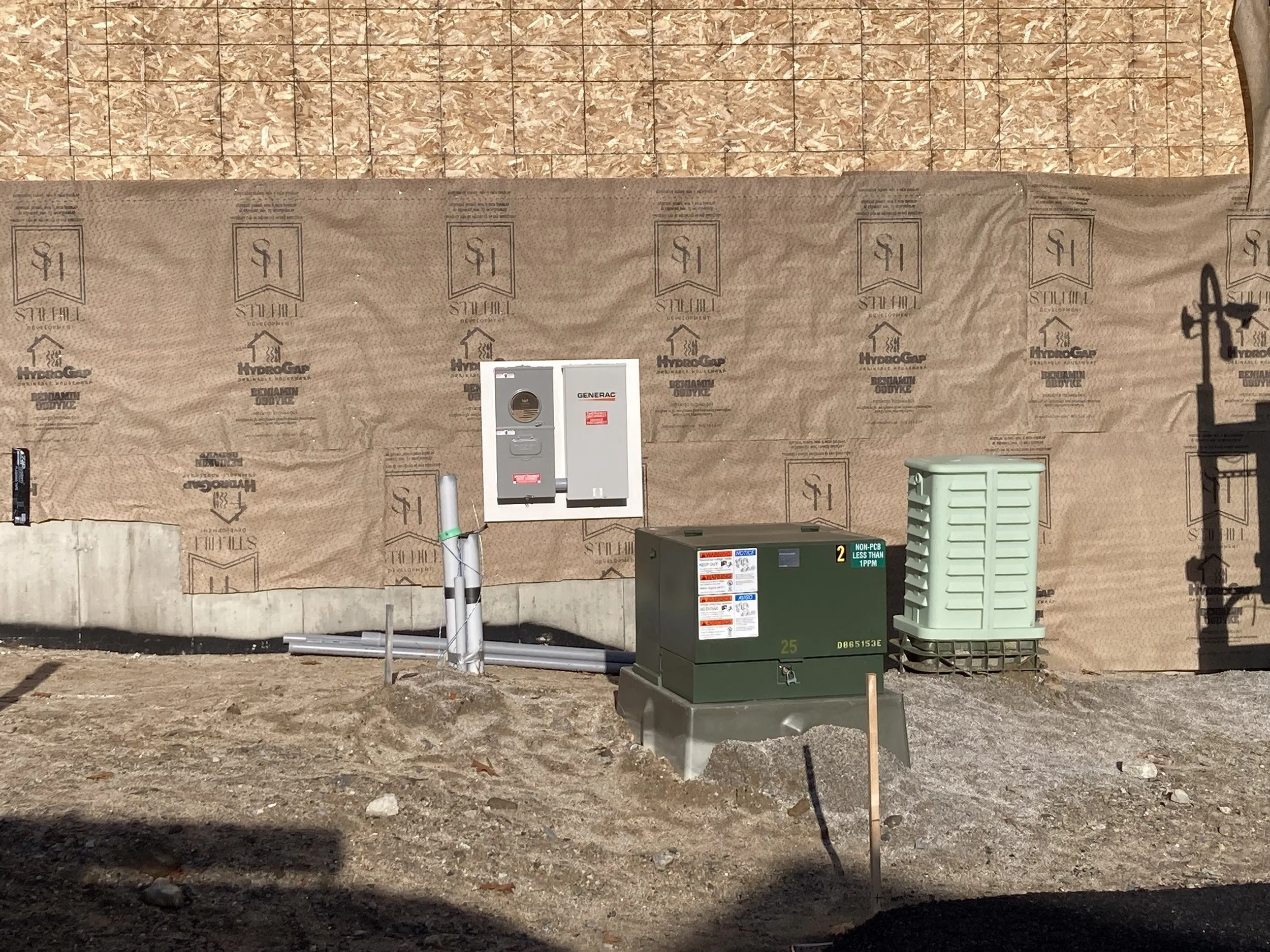 Construction site with a wood-paneled wall, electrical meters, and an HVAC unit in the foreground.