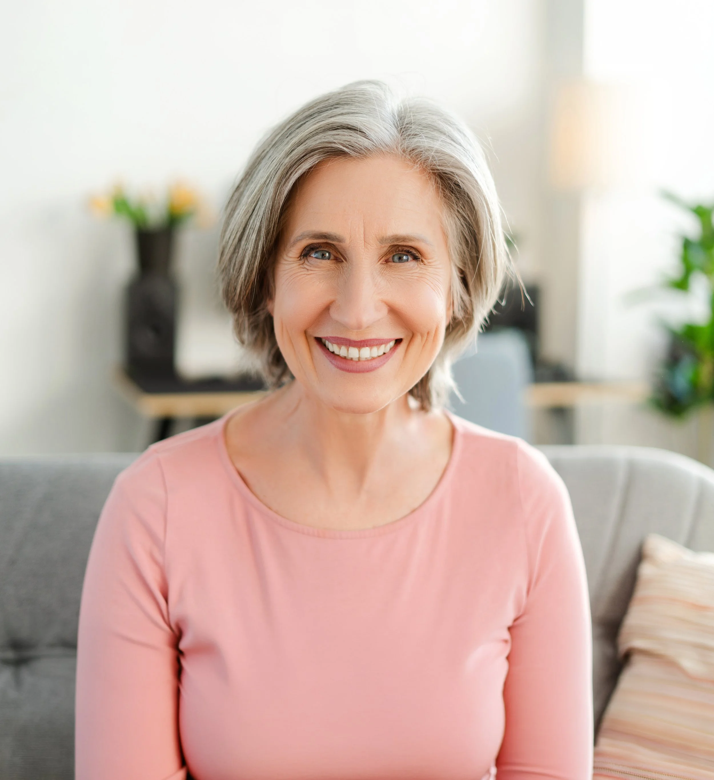 Woman with straight grey hair, smiling, wearing a pink shirt.