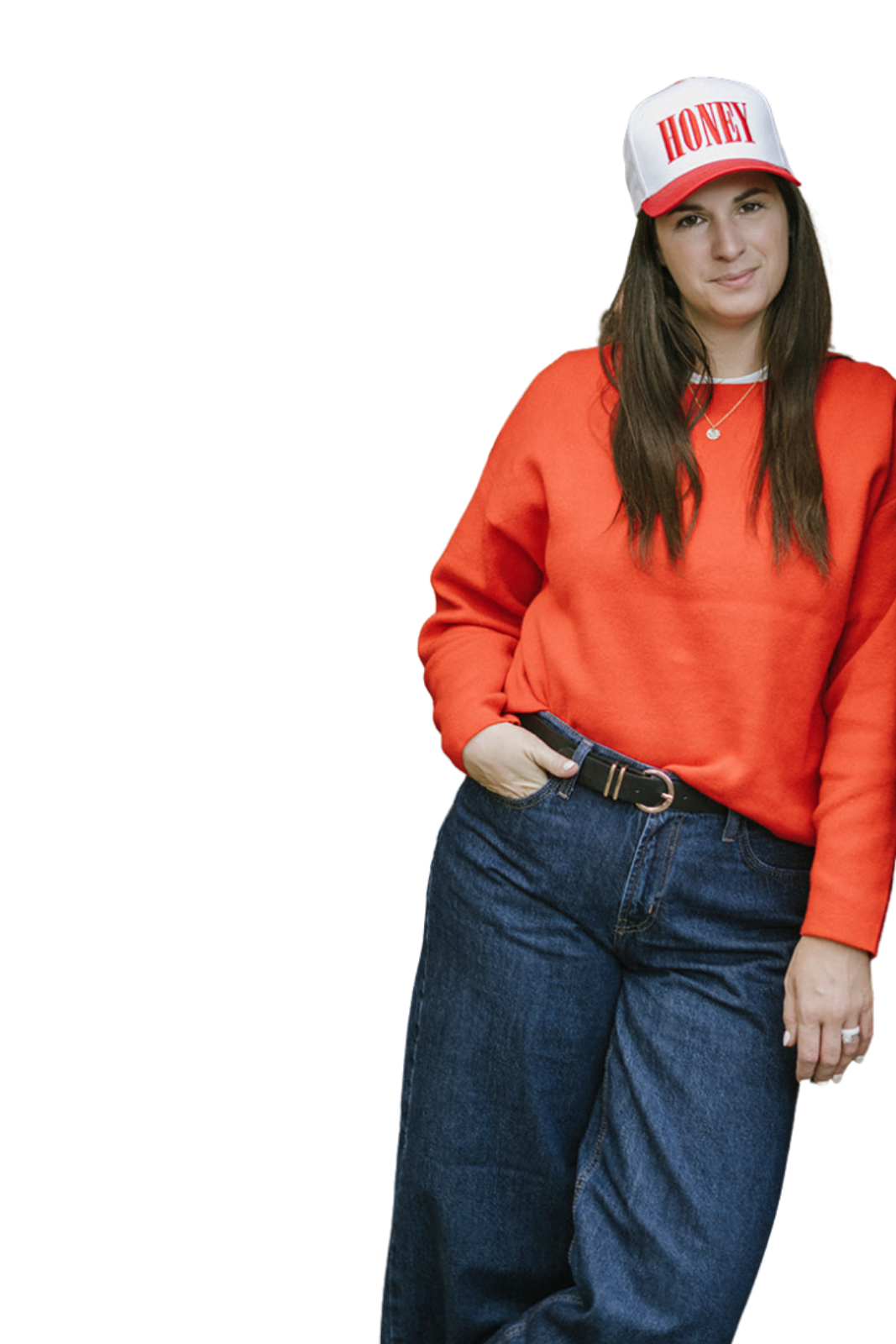 A woman wearing a white and red cap with the word 'HONEY', a red sweatshirt, and blue jeans is standing with one hand in her pocket and looking at the camera.