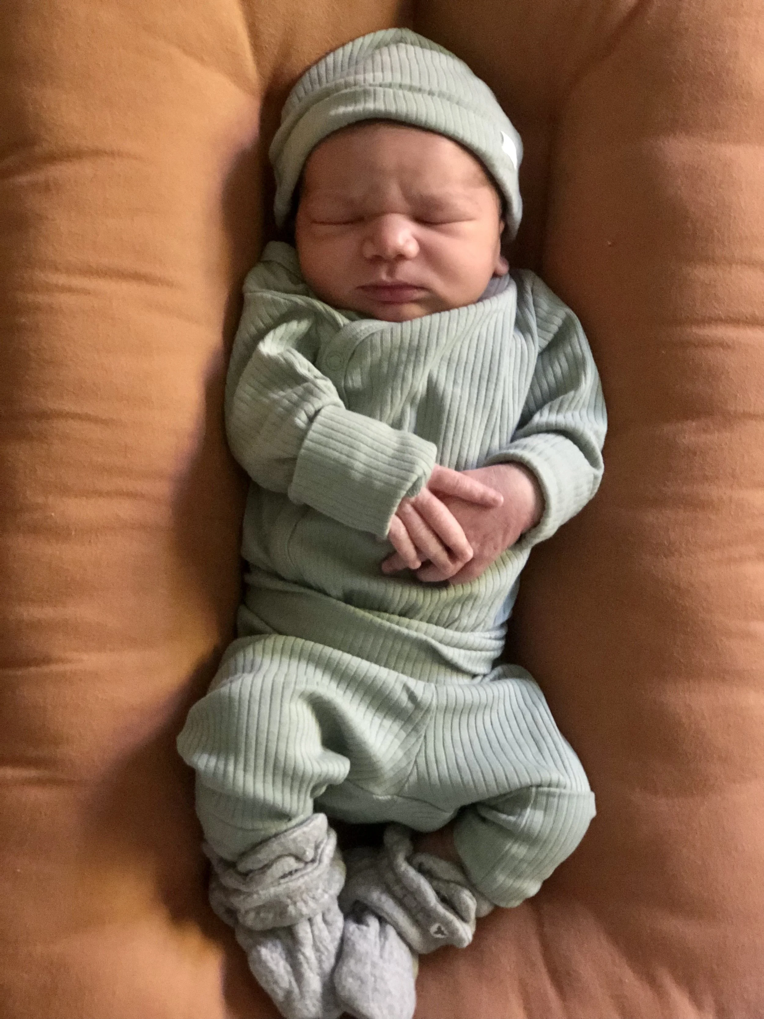 Newborn baby in green outfit and hat, lying down.
