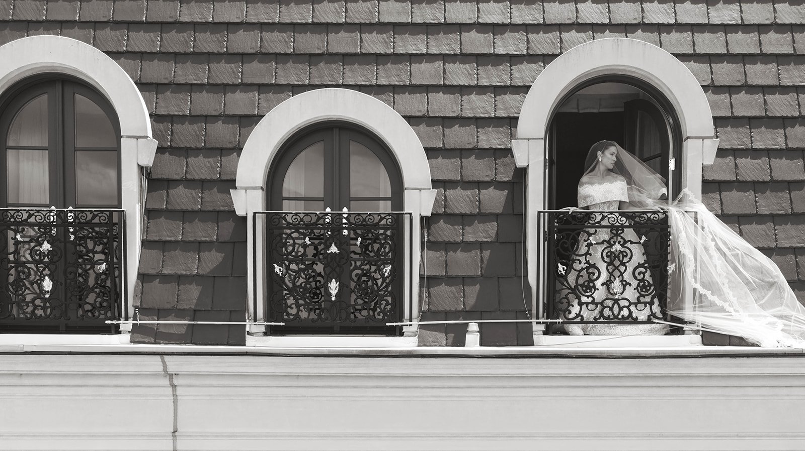 Bride and bridesmaids in light dresses holding bouquets stand in front of a floral arch outdoors.