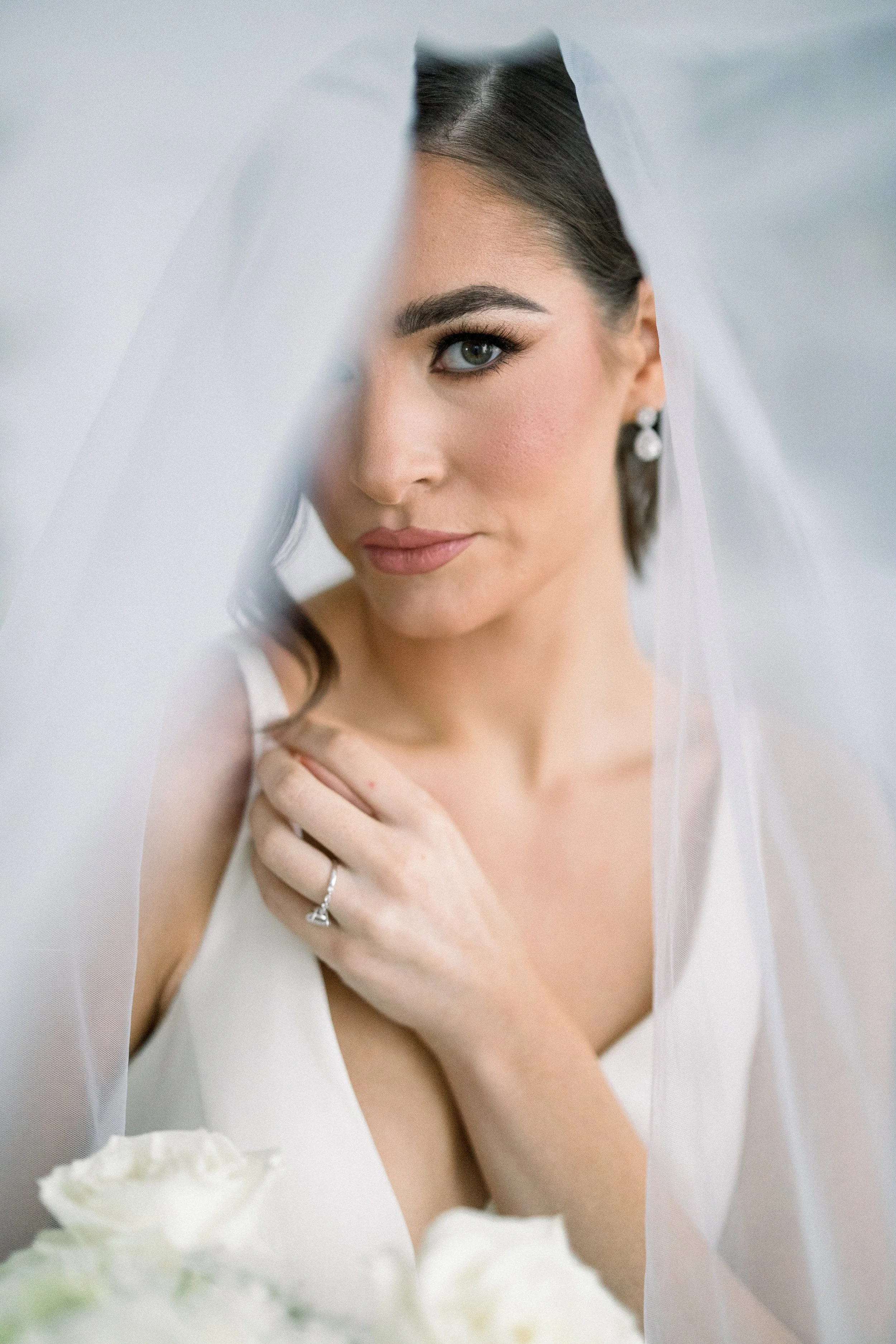 Bride under veil holding bouquet, displaying engagement ring.