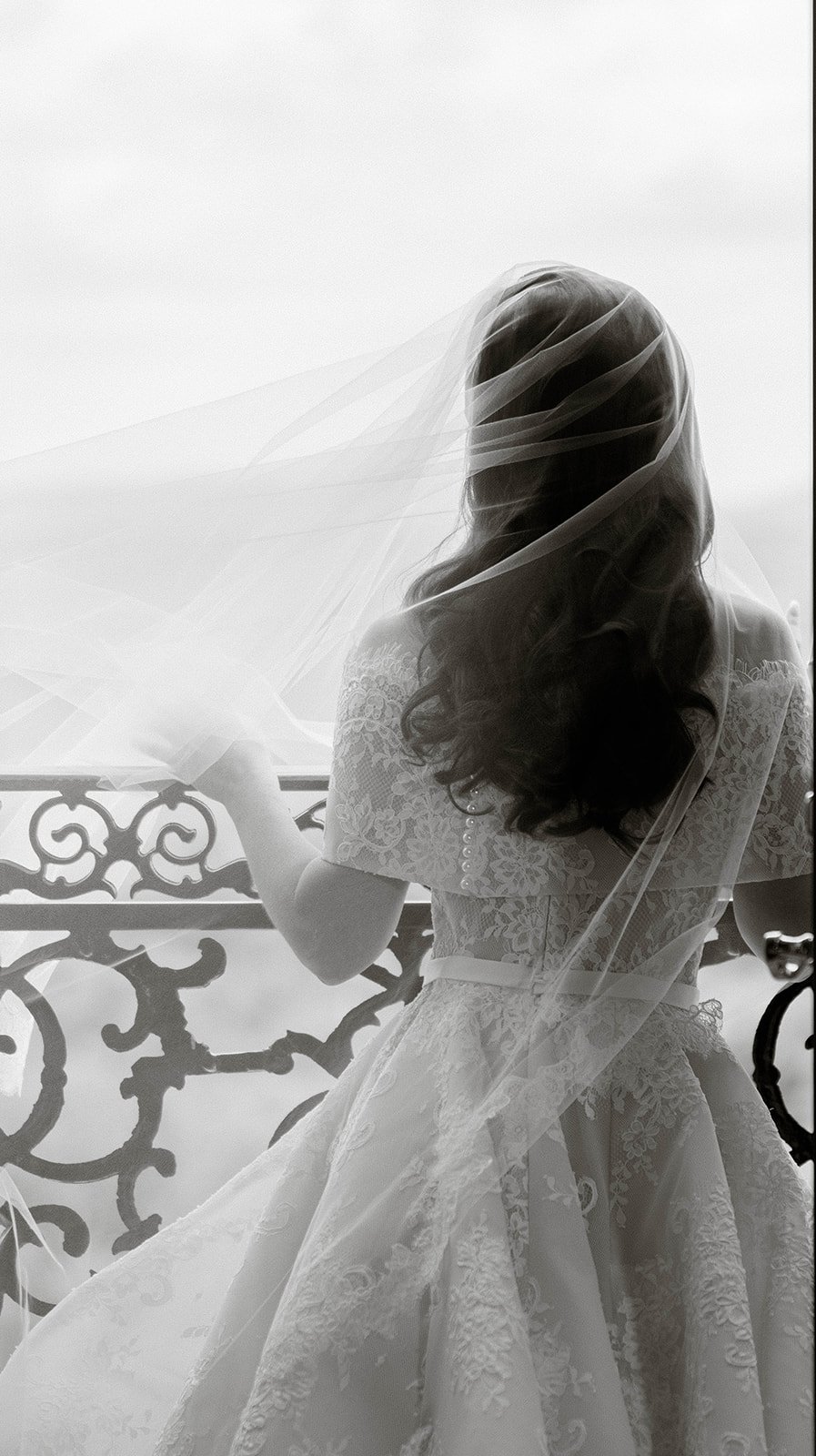 Bride and groom embracing, she holds a champagne glass, near a champagne tower and parasol.