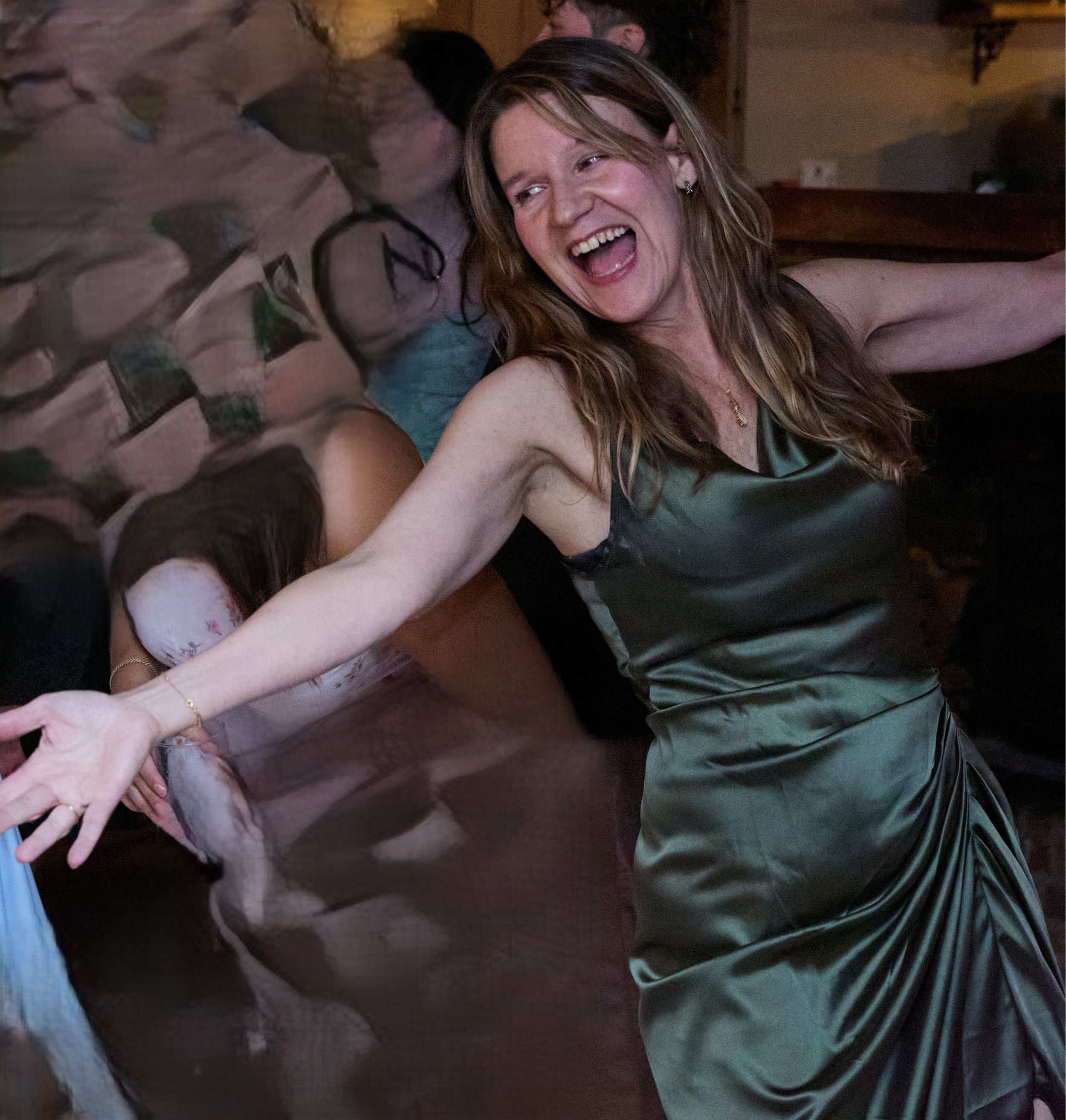 A woman dancing, smiling with her arms outstretched in a lively setting with blurred background of other people.